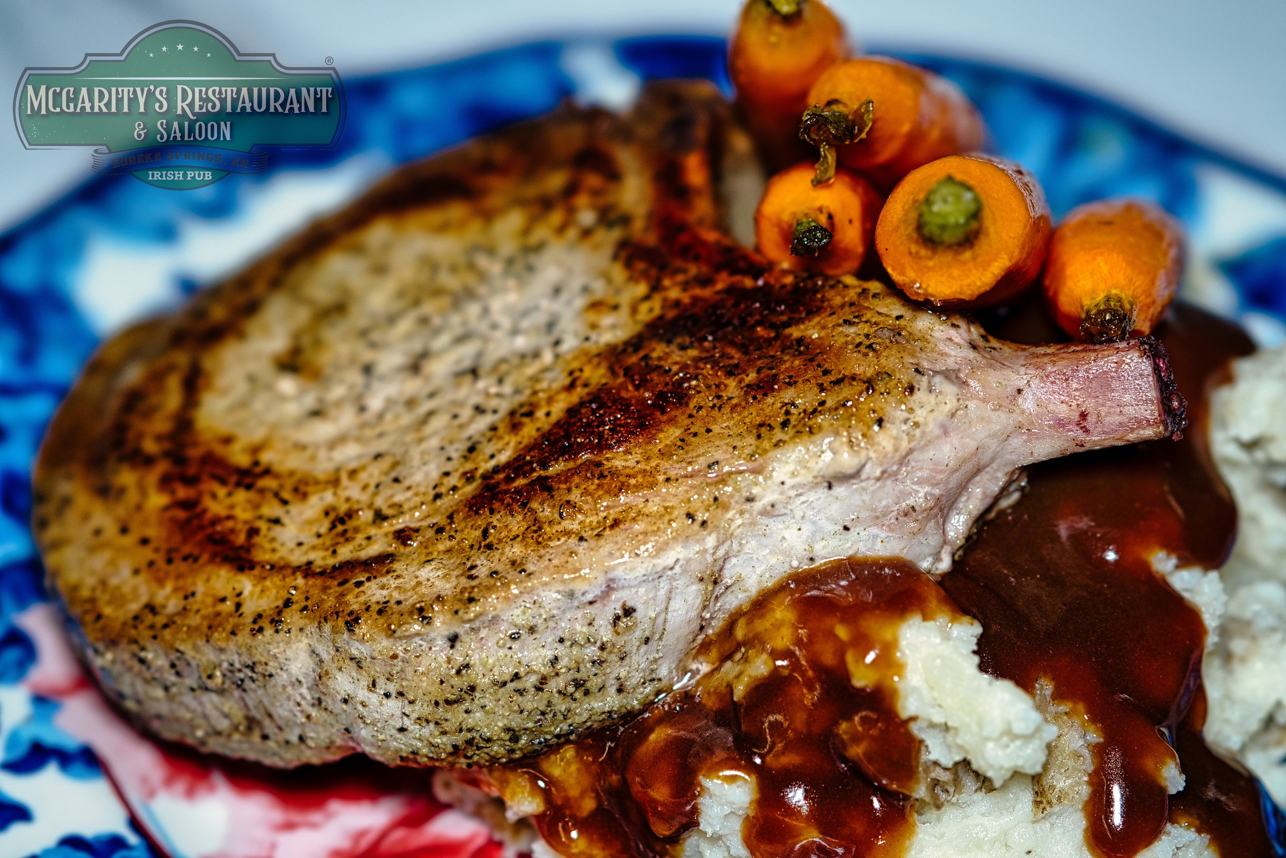 A plate of roasted pork chop with gravy, mashed potatoes, and roasted carrots, served on a decorative plate at McGarity's Restaurant and Saloon.