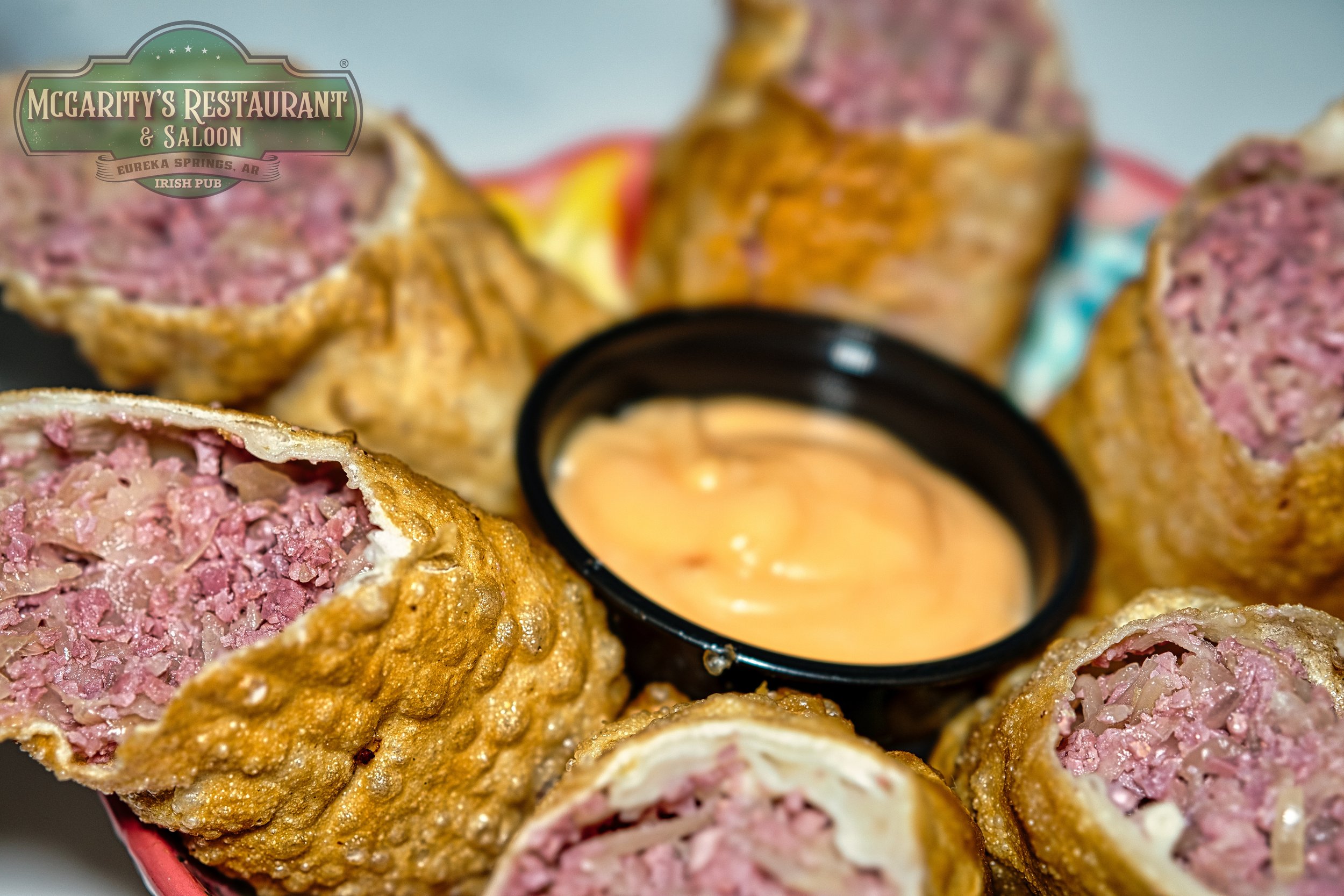A plate of deep-fried sausage rolls arranged around a small black bowl of dipping sauce, with the McGarity's Restaurant & Saloon logo in the upper left corner.