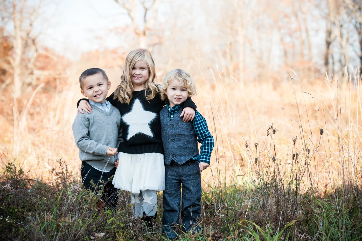 Three young siblings hugging in a fall field