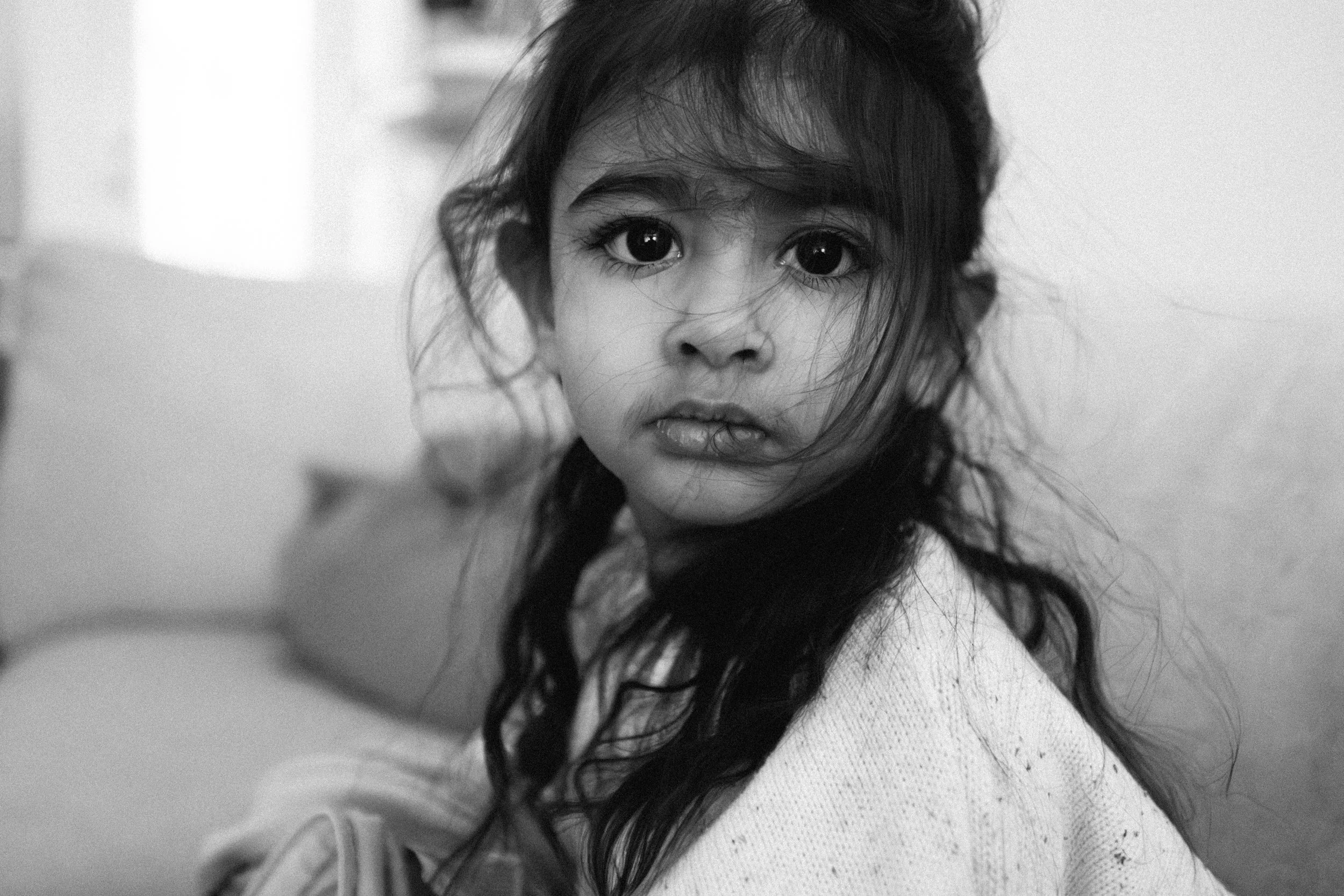Black and white photo of a young girl with long hair, looking directly at the camera with a curious expression.