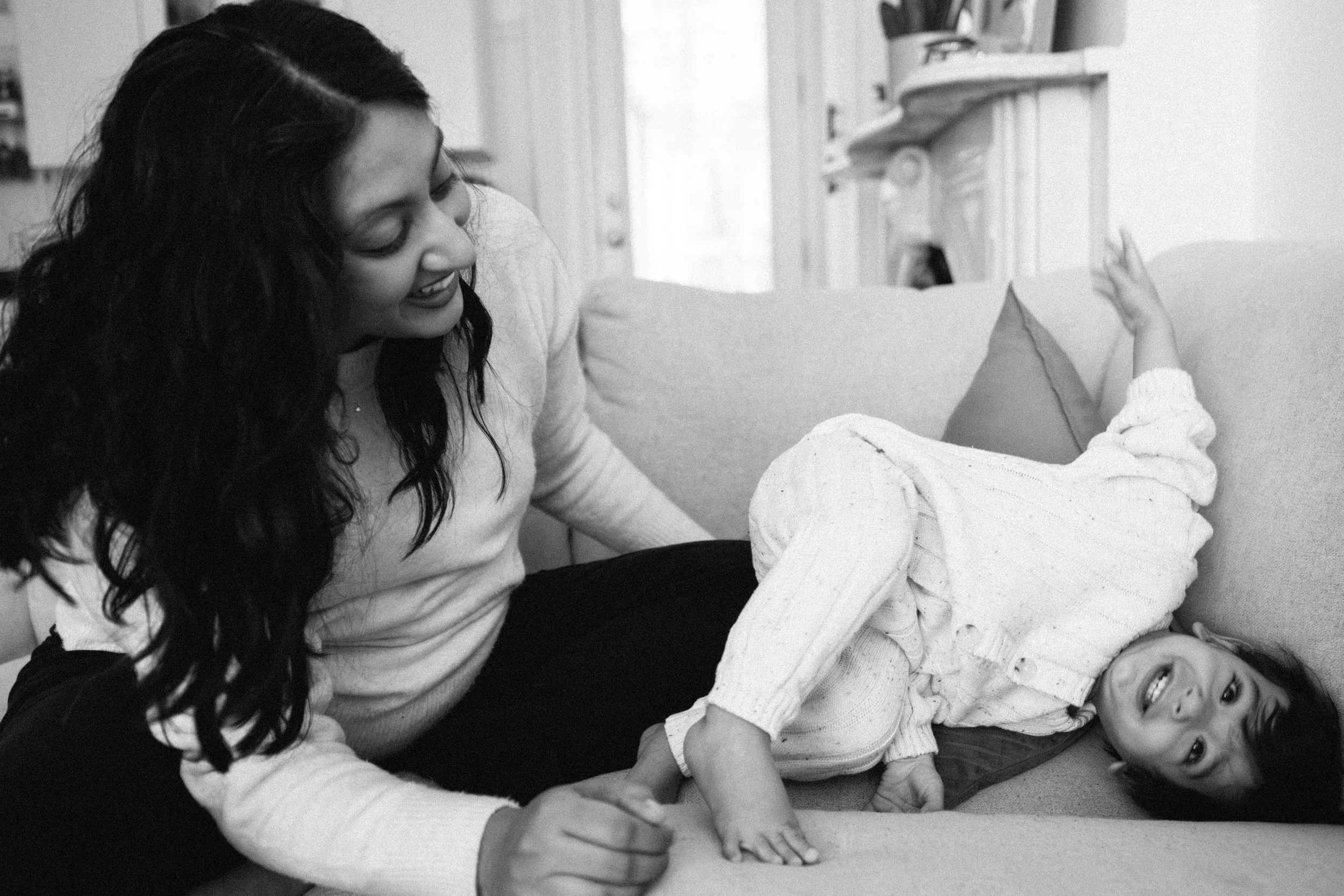 A woman and a young girl playing on a couch, smiling and laughing together.