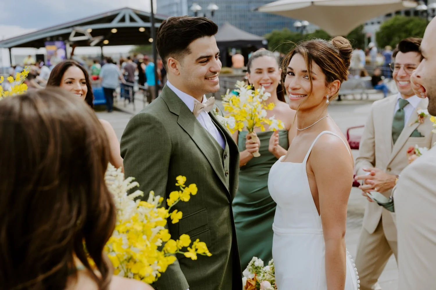 Wedding couple smiling at each other surrounded by bridesmaids and groomsmen outdoors.