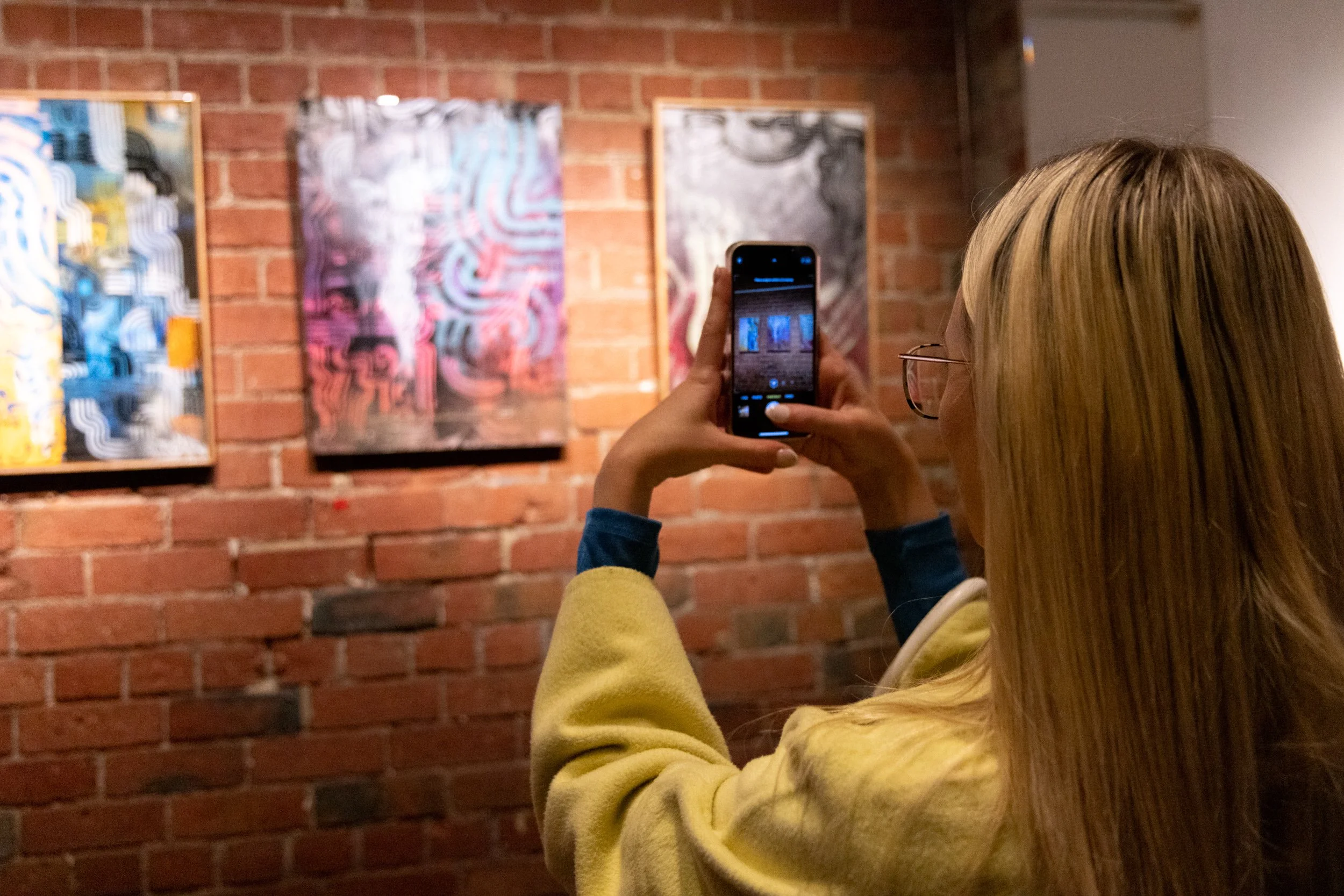 Photograph of visitor viewing artwork through their phone. Artwork created by Bailer at Let's Pretend Gallery. The image is from Melbourne Graffiti Artist Bailer's opening night for their solo exhibition titled 'Mixed Messages'.