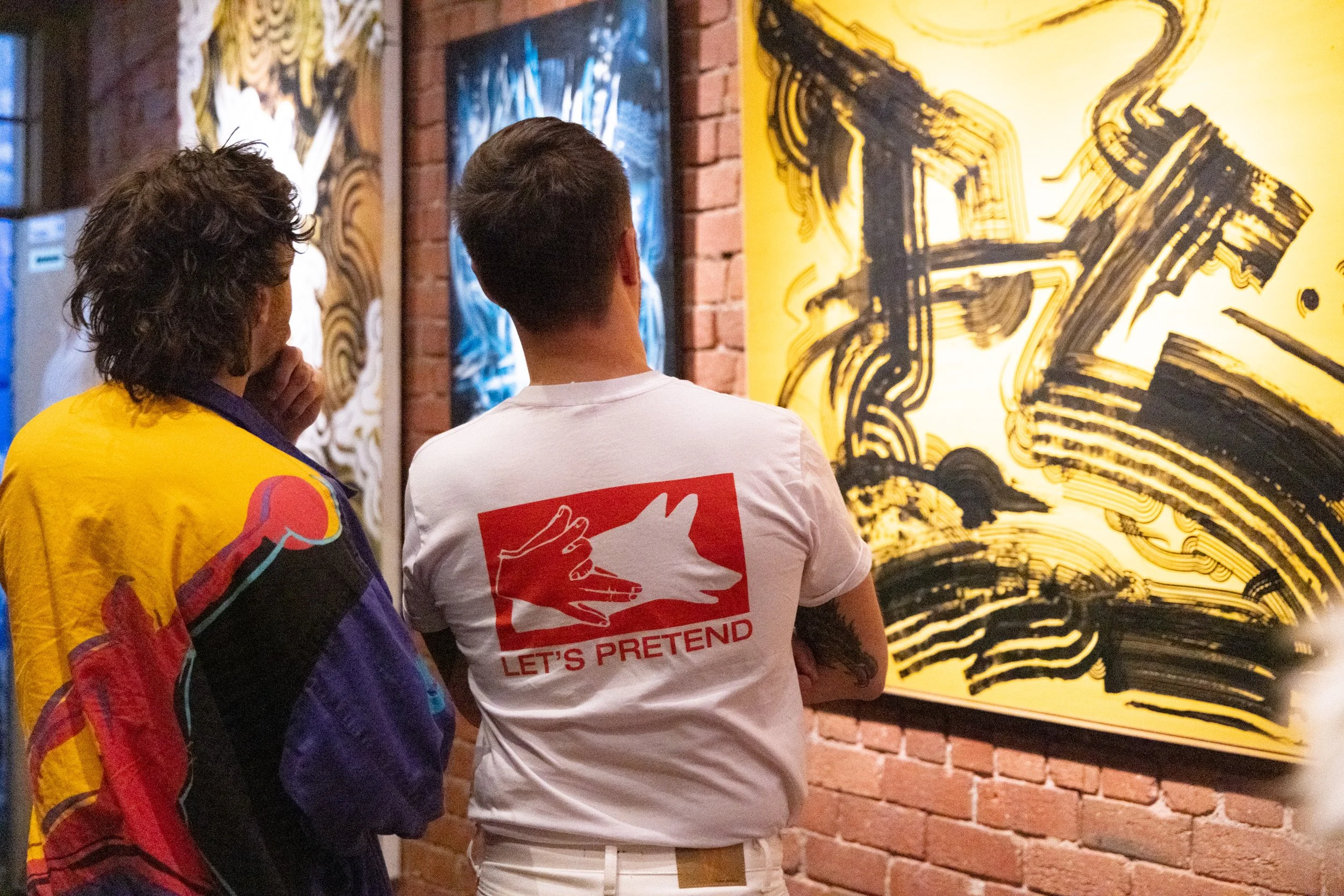 Photograph of two visitors looking at the artworks of Bailer. The image is from Melbourne Graffiti Artist Bailer's opening night for their solo exhibition titled 'Mixed Messages'.