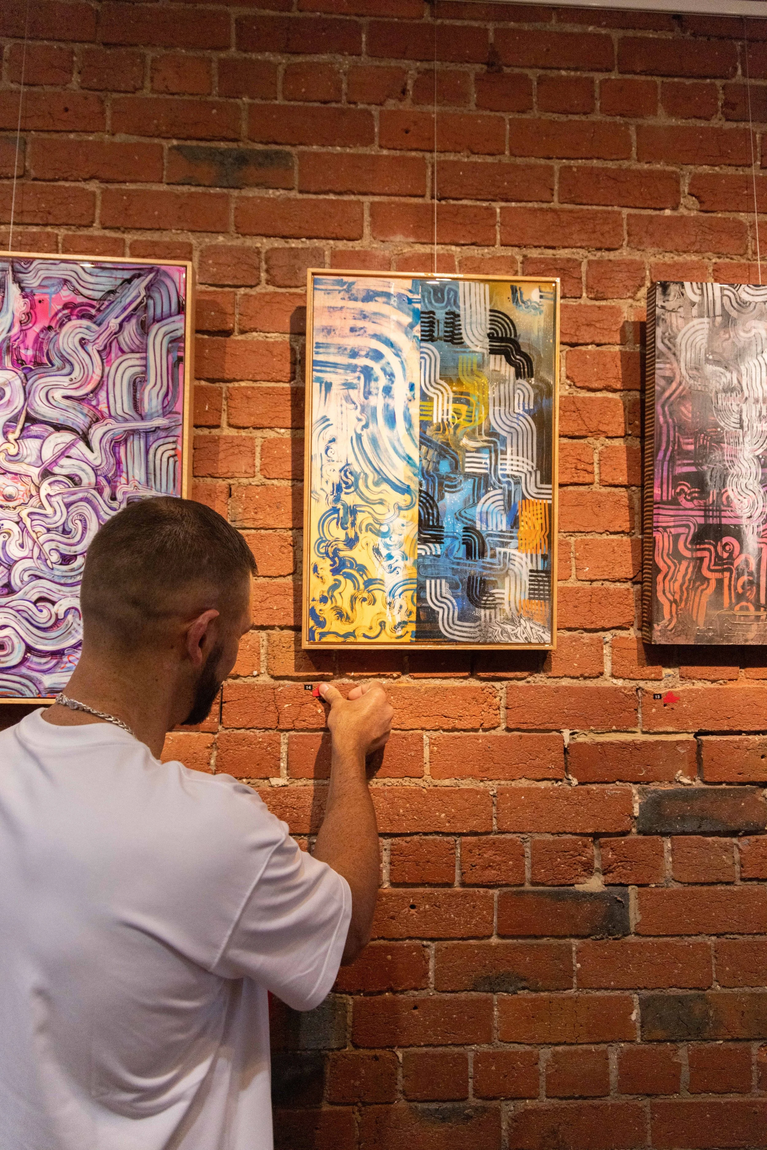 Photograph of red sold sticker being placed underneath an artwork by Bailer at Let's Pretend Gallery. The image is from Melbourne Graffiti Artist Bailer's opening night for their solo exhibition titled 'Mixed Messages'.