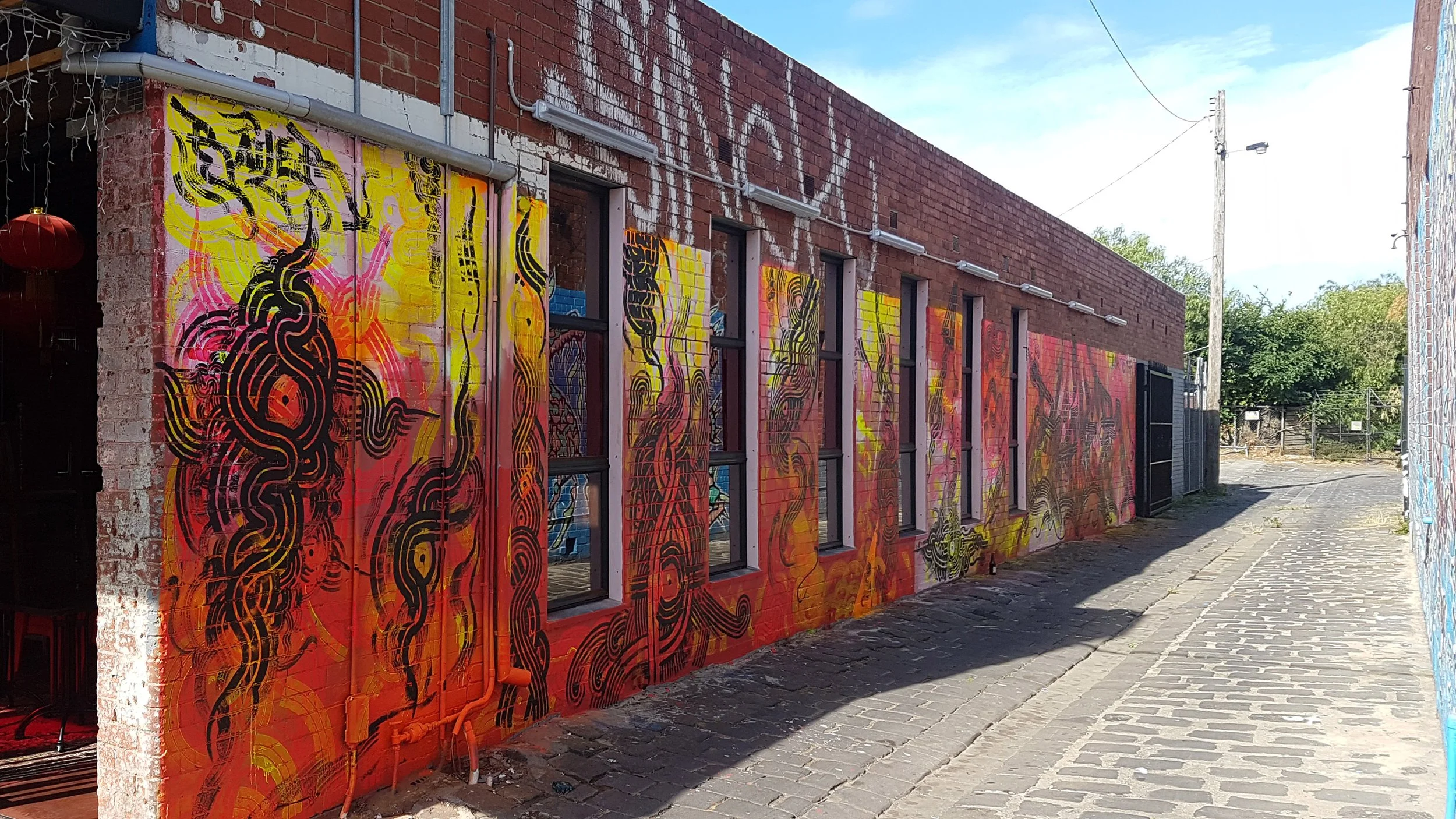 Multiroller, Chapel Street: Chapel Street restaurant mural by Melbourne graffiti artist Bailer, featuring black Multiroller forms over a bright fluorescent orange and warm-toned background.