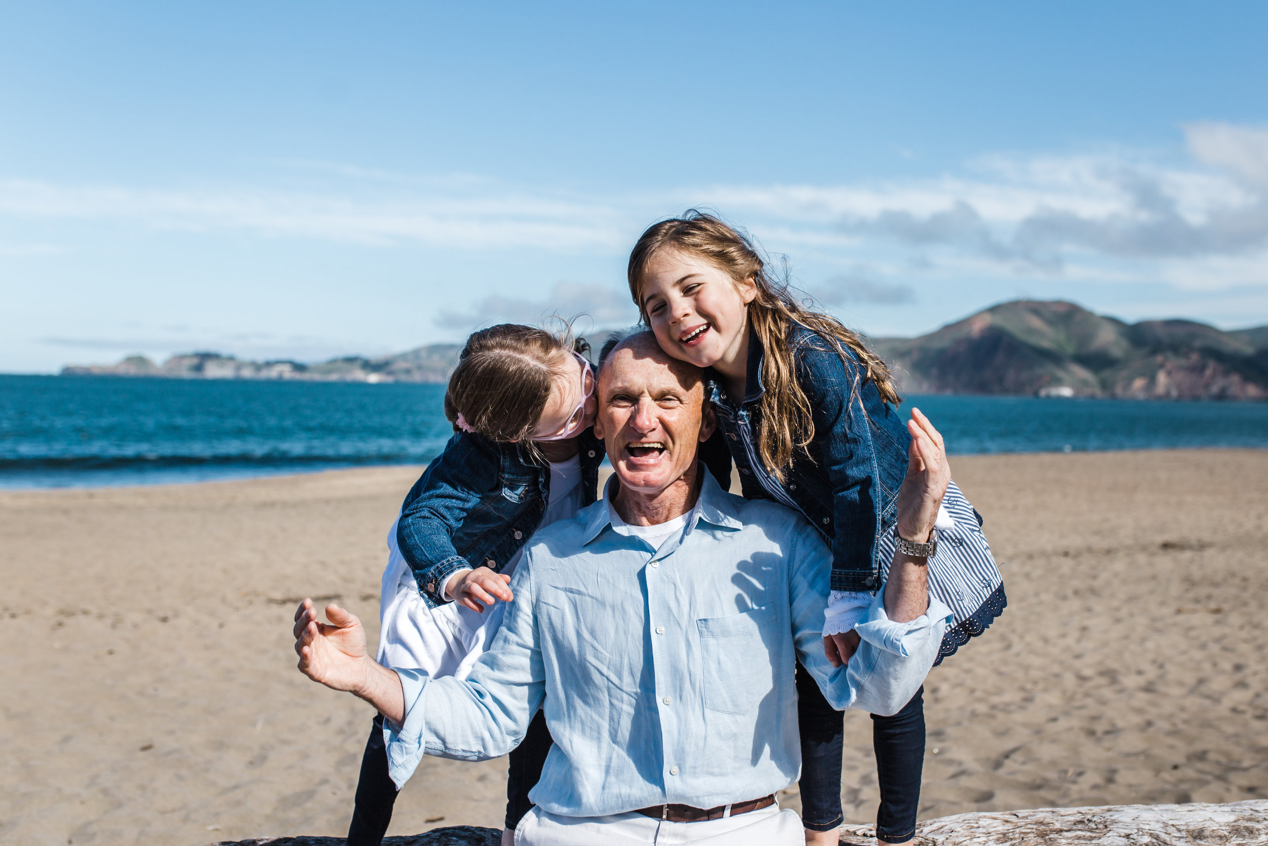 dad sitting on the beach with his twin five year old girls while girls each hug and kiss him from either side of him {Bay Area Family Photography}