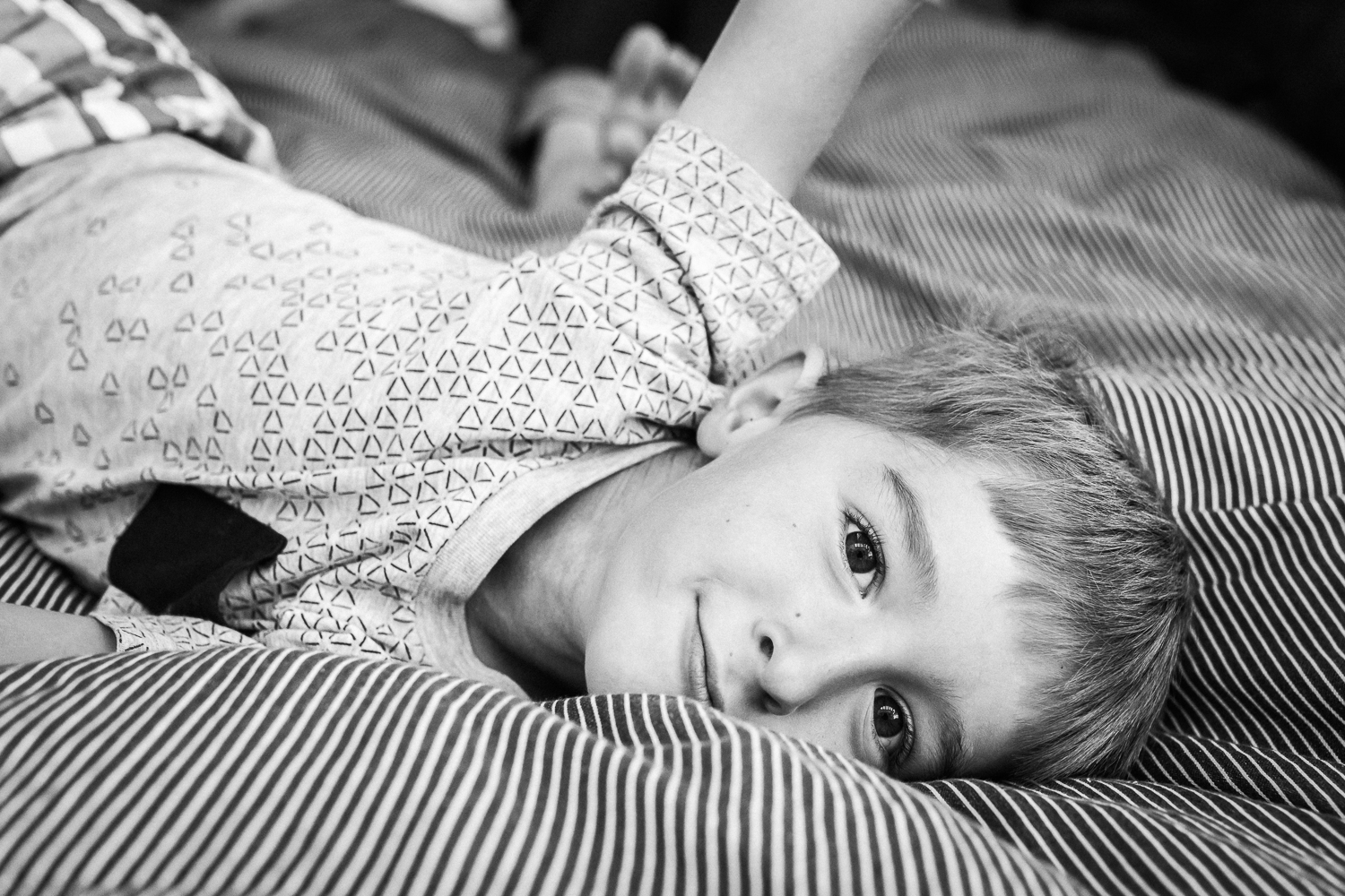  five year old boy laying on his parent’s bed and smiling at the camera {San Francisco in-home Family Photographer}