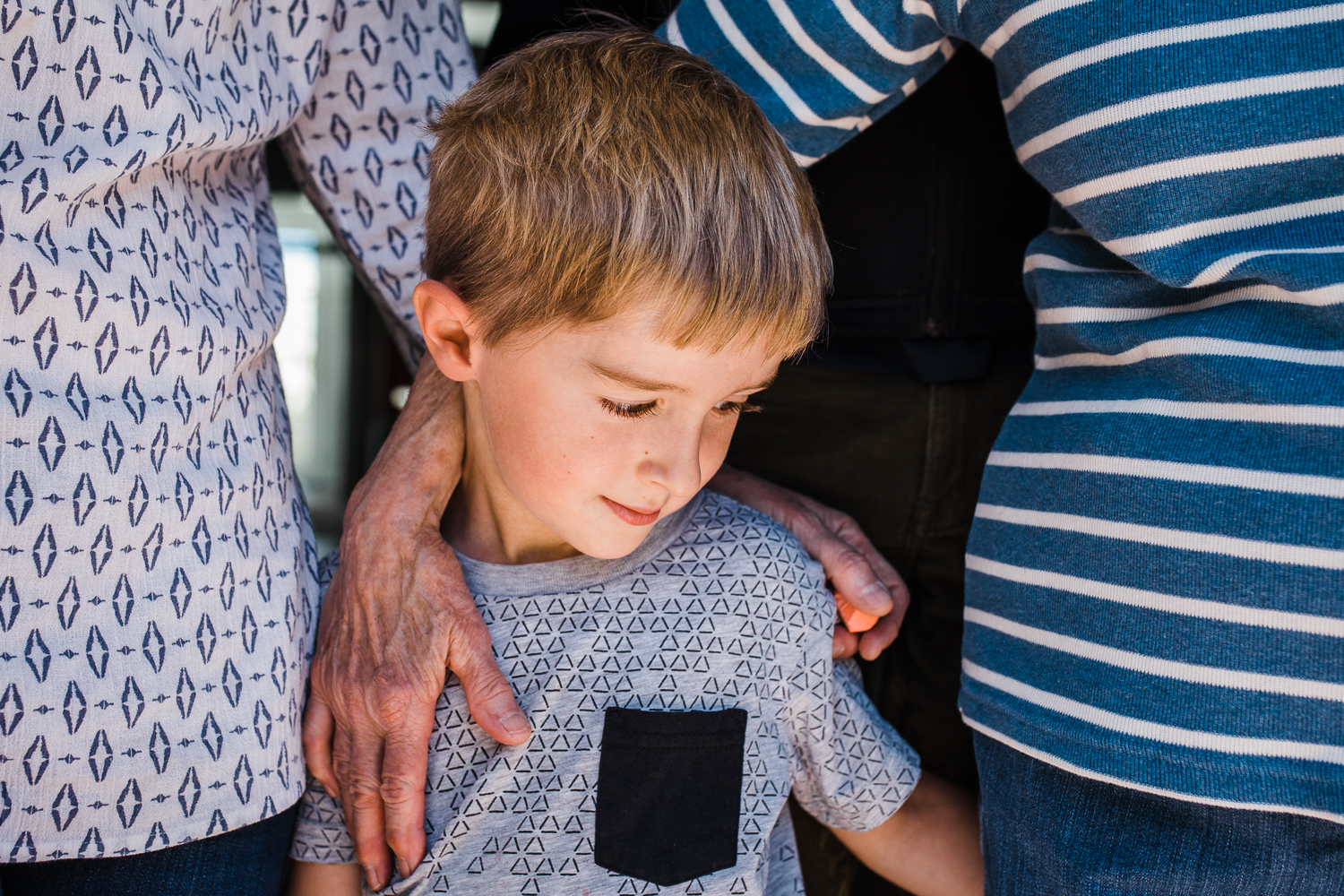 close up of five year old boy standing next to his mother and grandmother with their hands touching his back {San Francisco in-home Family Photographer}