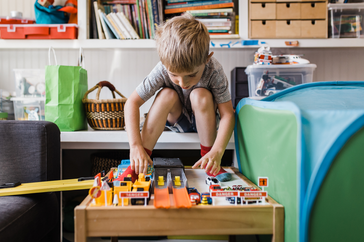 five year old boy sitting on a shelf while playing with his cars - his feet propped up on lego table {San Francisco in-home Family Photographer}