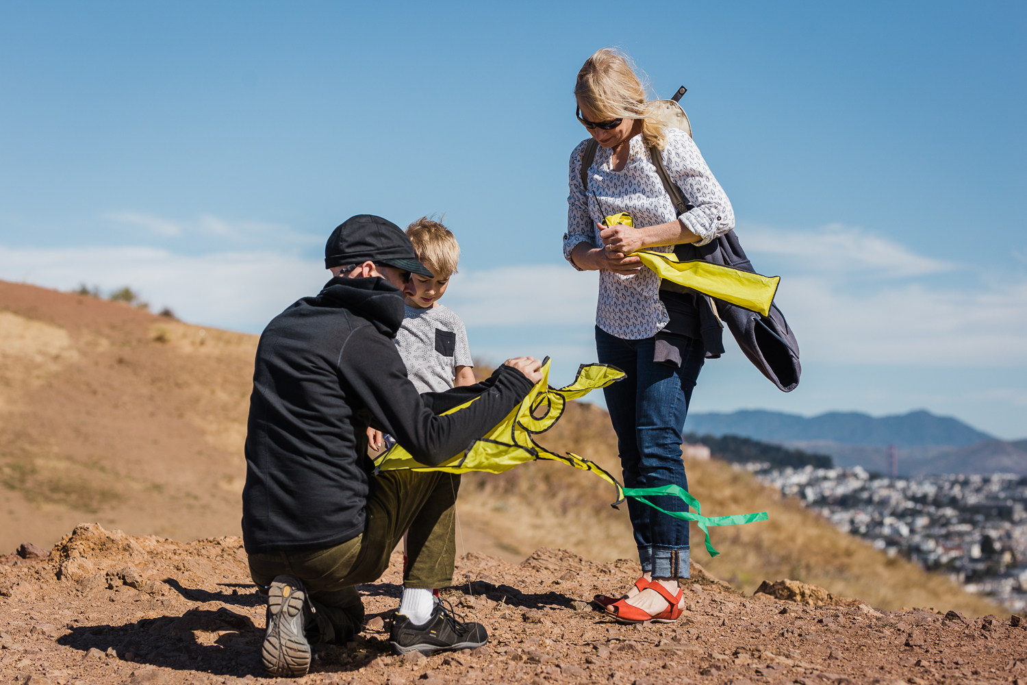 Family of three setting up to fly a kite overlooking the city {San Francisco Lifestyle Photographer}