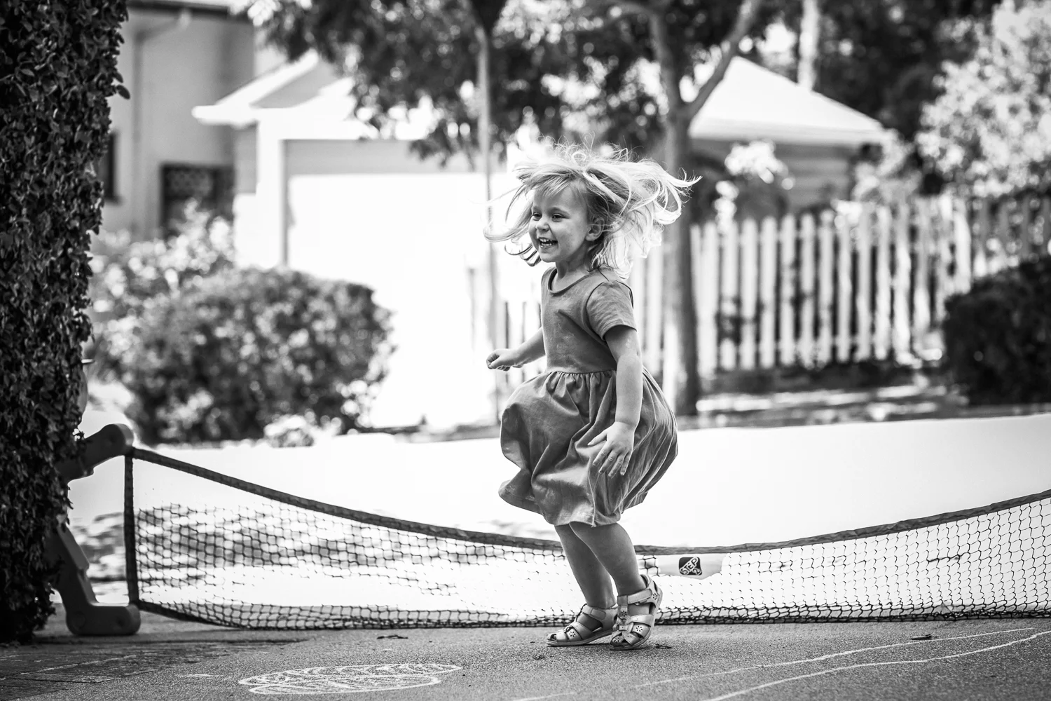 black and white photo of a three year old little girl jumping on the driveway of her house {Oakland in-home lifestyle Family Photographer}