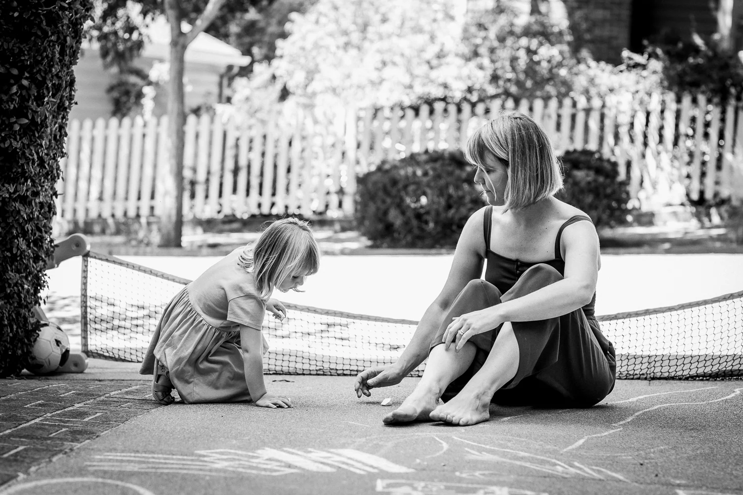 black and white picture of mom and three year old daughter drawing with sidewalk chalk on the driveway of their house {Oakland in-home lifestyle Family Photographer}