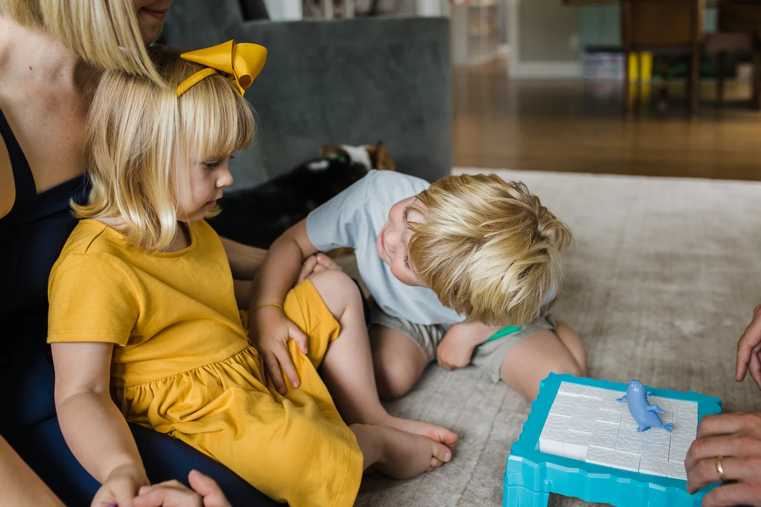 five year old brother looking at his two year old sister trying to get her attention while they are playing a game together with Mom and Dad {Oakland in-home lifestyle Family Photographer}