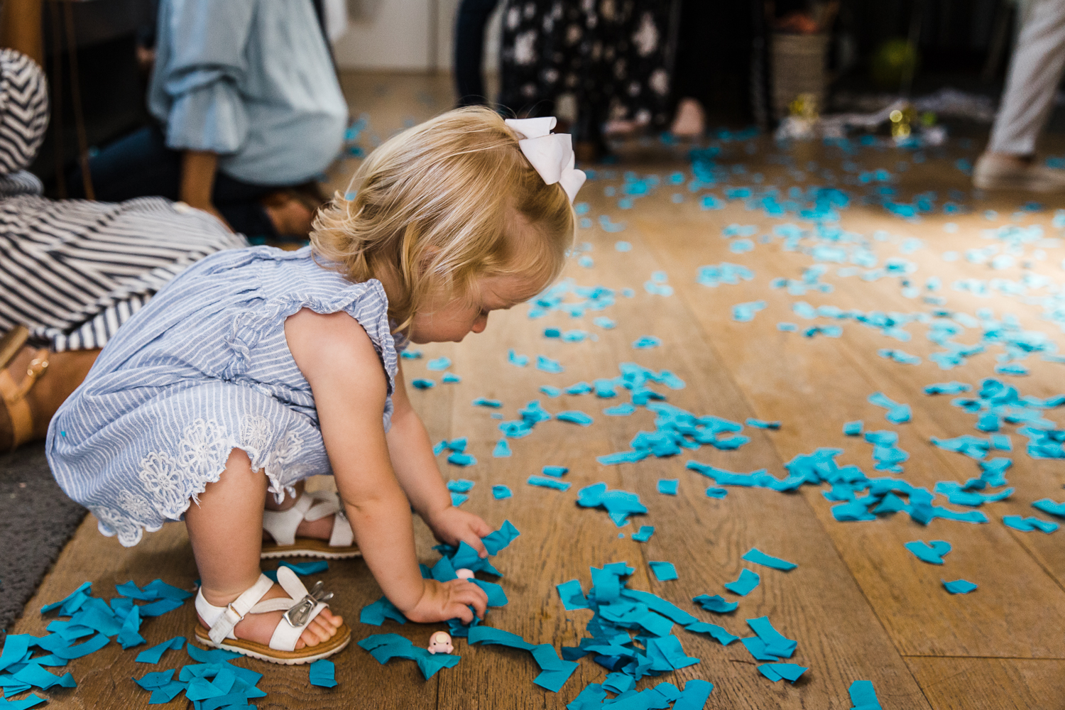 A two year old girl playing with blue confetti on the floor after a gender reveal party {San Francisco Family Photographer}