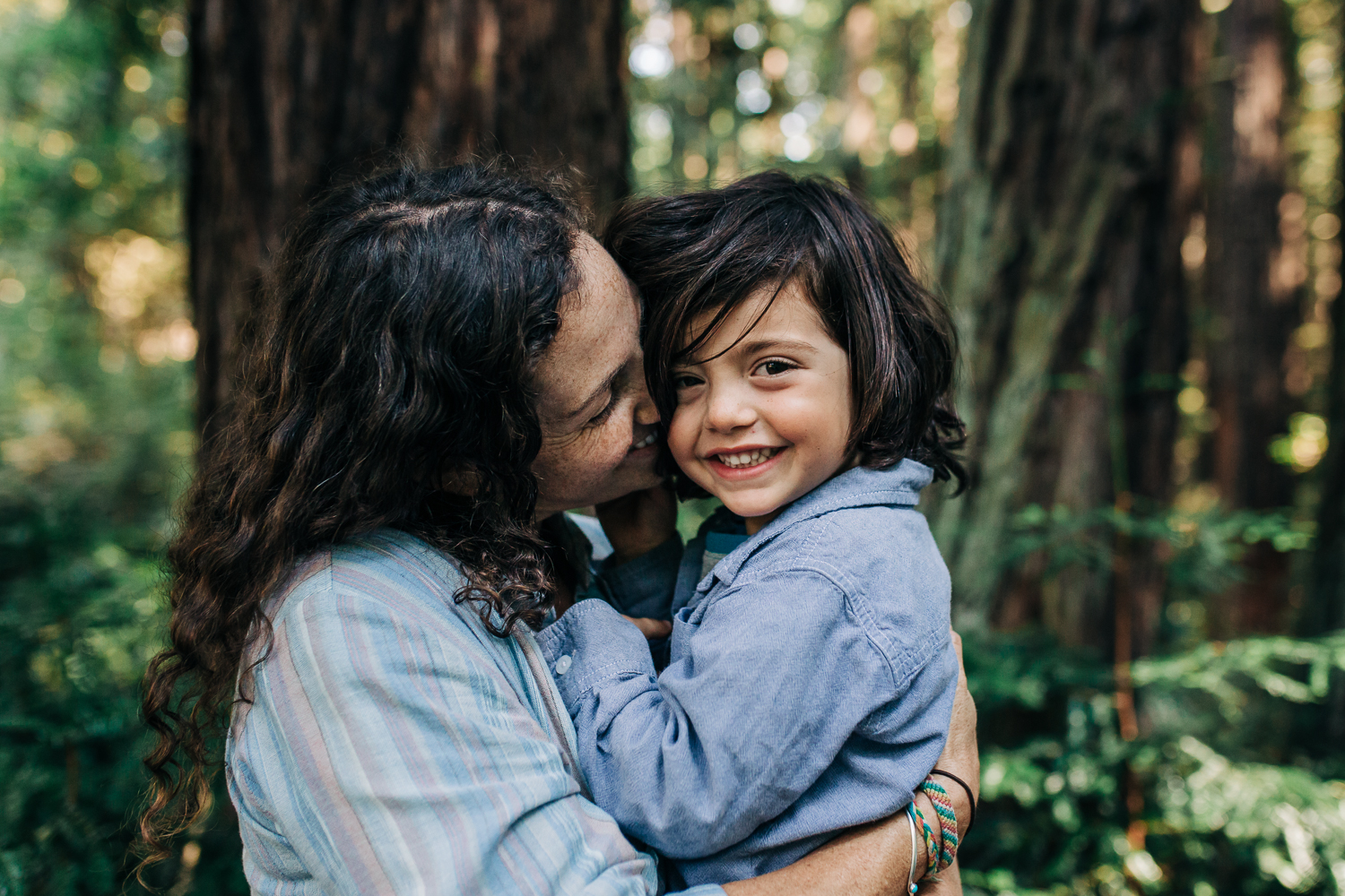 Mom snuggling her four year old boy as he looks at the camera and smiles while in the woods {Oakland Family Photographer}