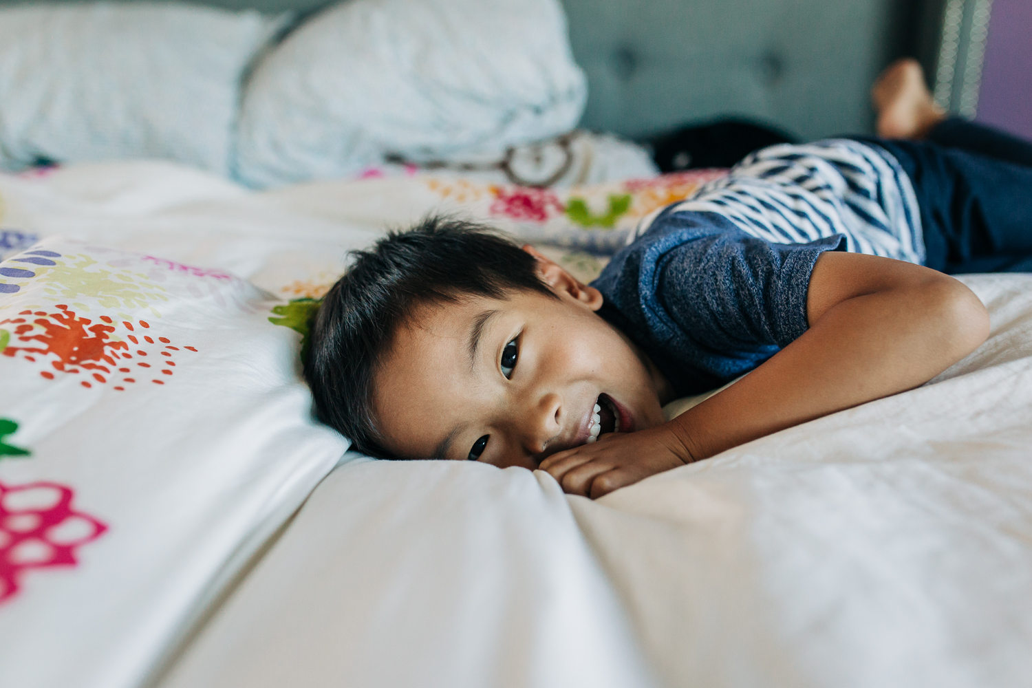 boy laying on a bed and looking and smiling at the camera | East Bay Lifestyle Family Photographer