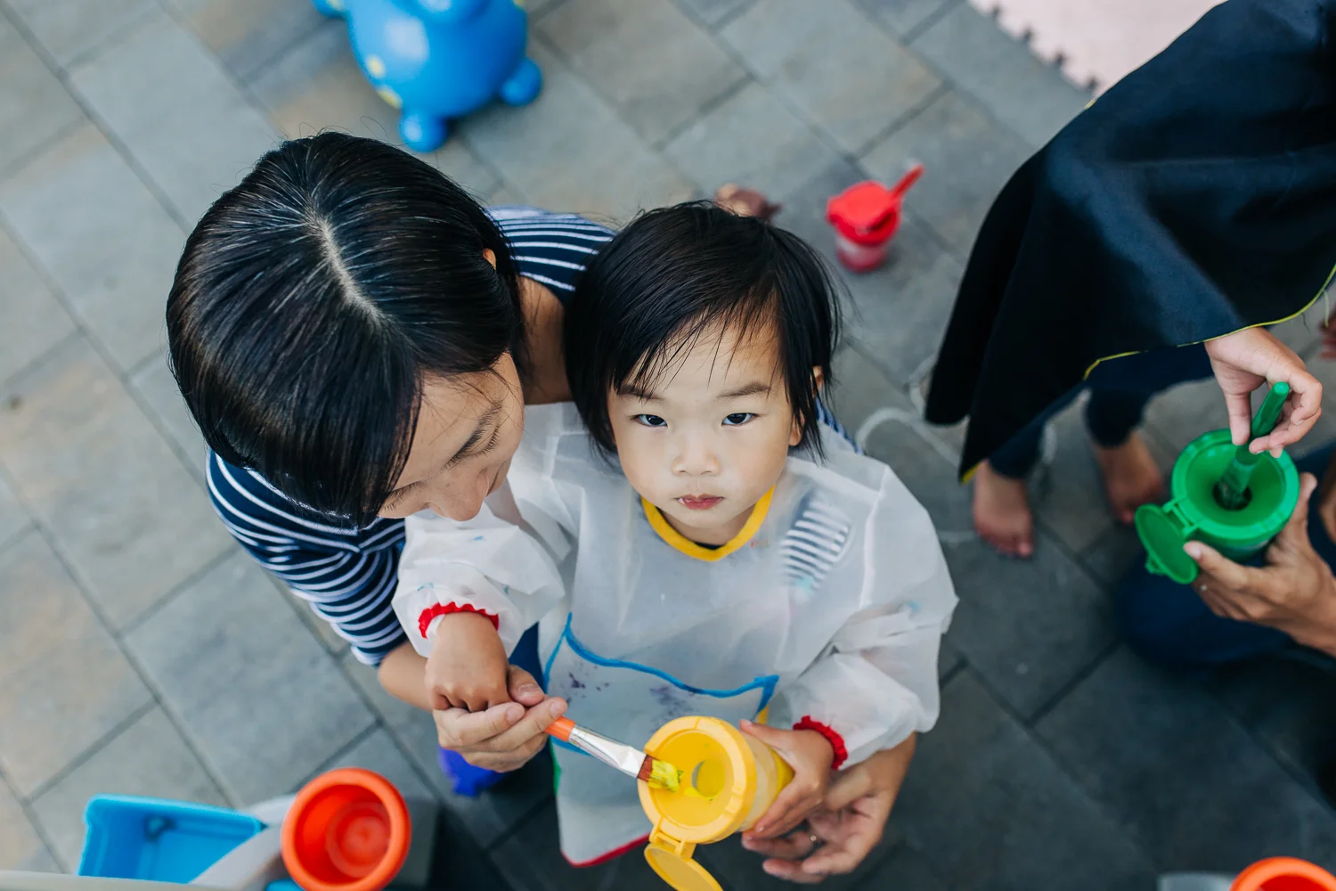 birds eye view of a two year old girl looking up while painting at an easel with her mother | East Bay Lifestyle Family Photographer