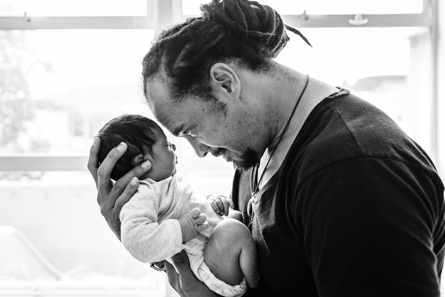 black and white shot of father holding his newborn baby boy to his forehead while standing in front of a window | San Francisco Fresh 48 Photographer
