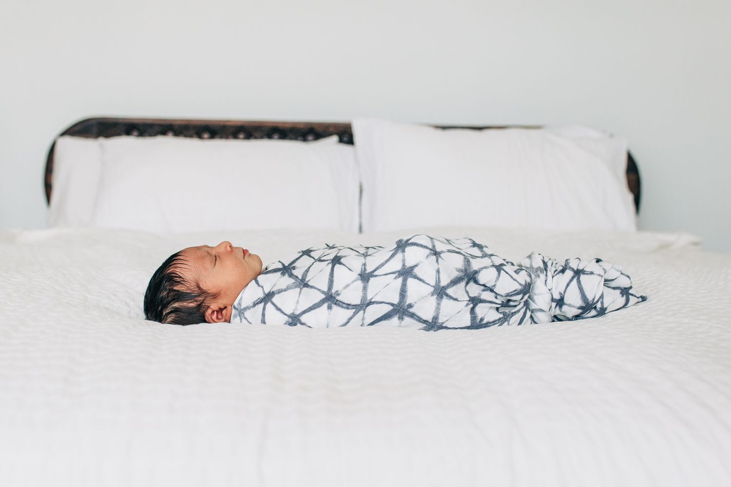 Swaddled baby boy sleeping across his parents white bed | San Francisco Newborn Photographer