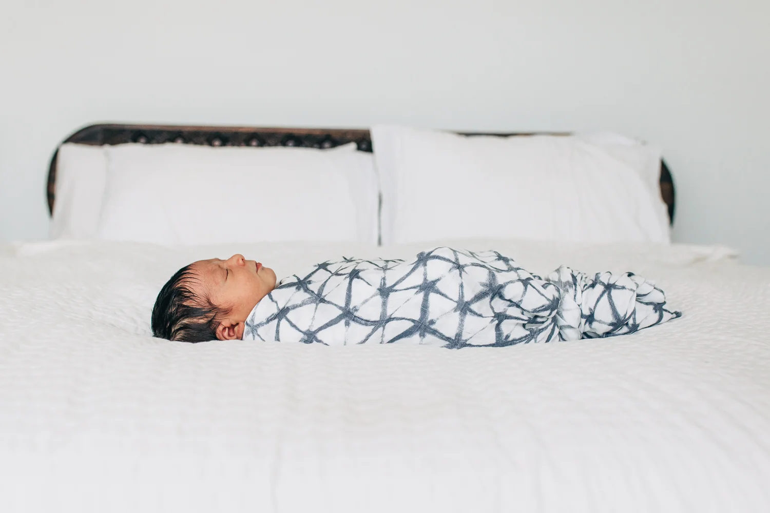 Swaddled baby boy sleeping across his parents white bed | San Francisco Newborn Photographer