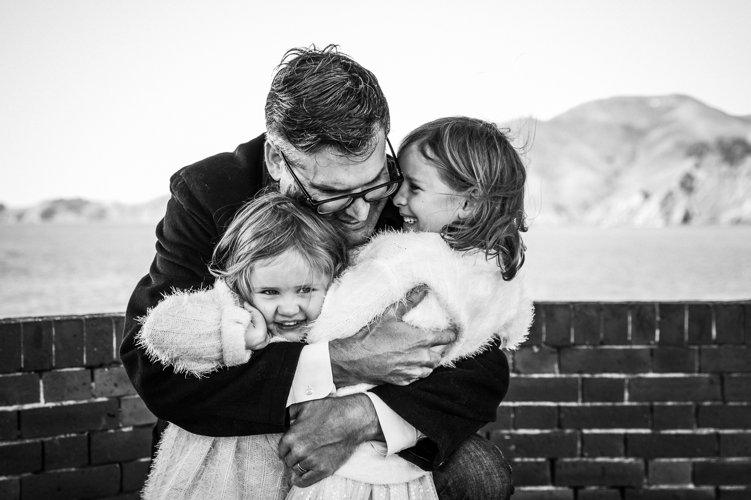 black and white photo of a dad hugging his two young girls while they smile {San Francisco Lifestyle Family Photographer}