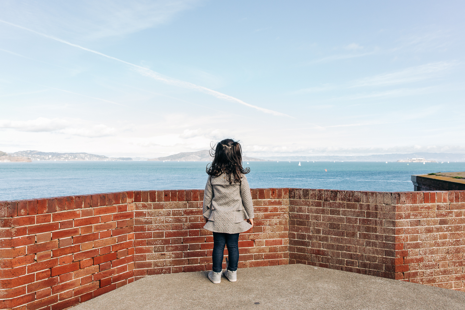 the back of a little girl standing at a brick wall and looking out at the bay {San Francisco Child Photographer}