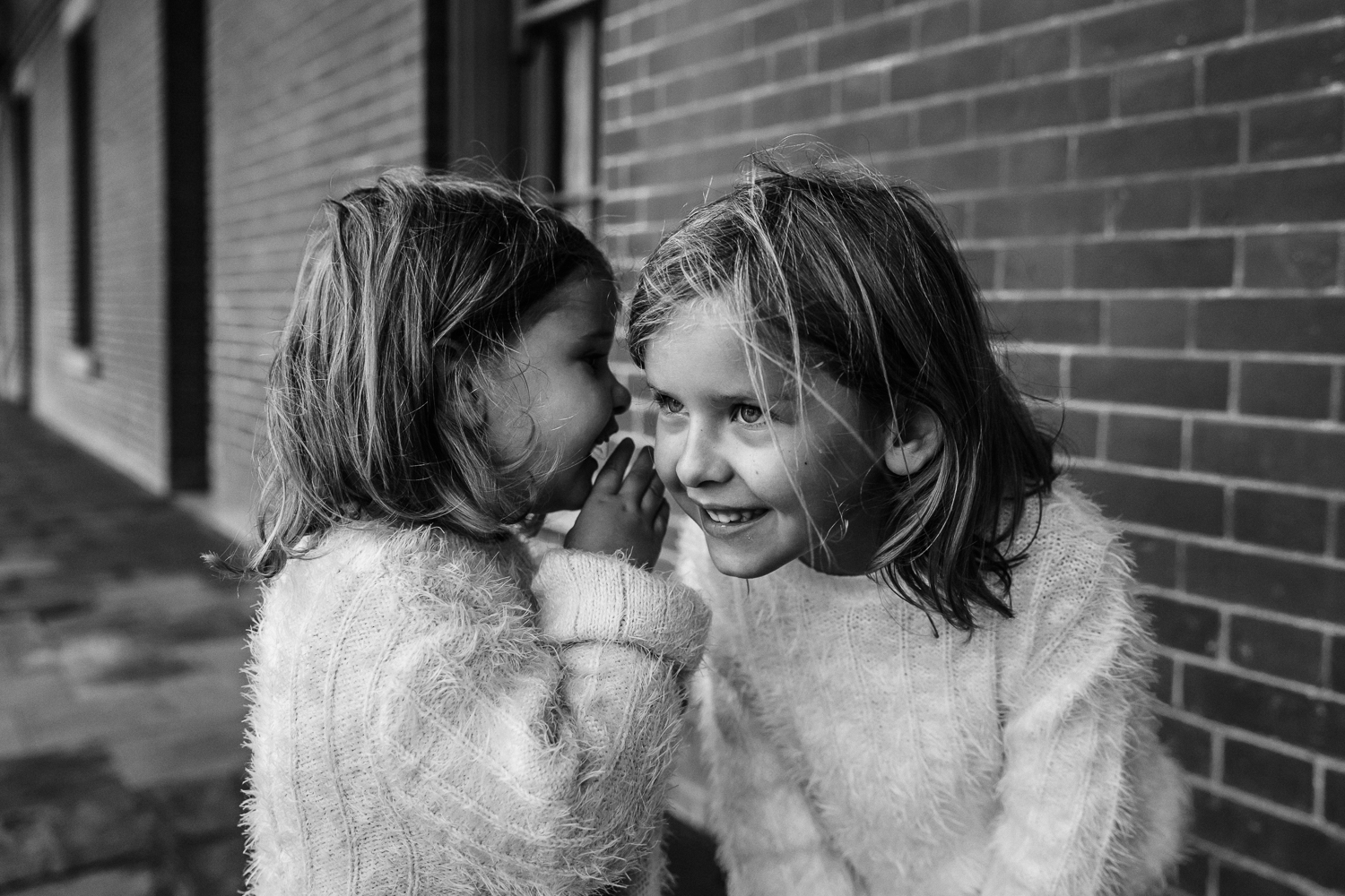 black and white photo of two sisters smiling and telling secrets with each other {East Bay Family Photographer}