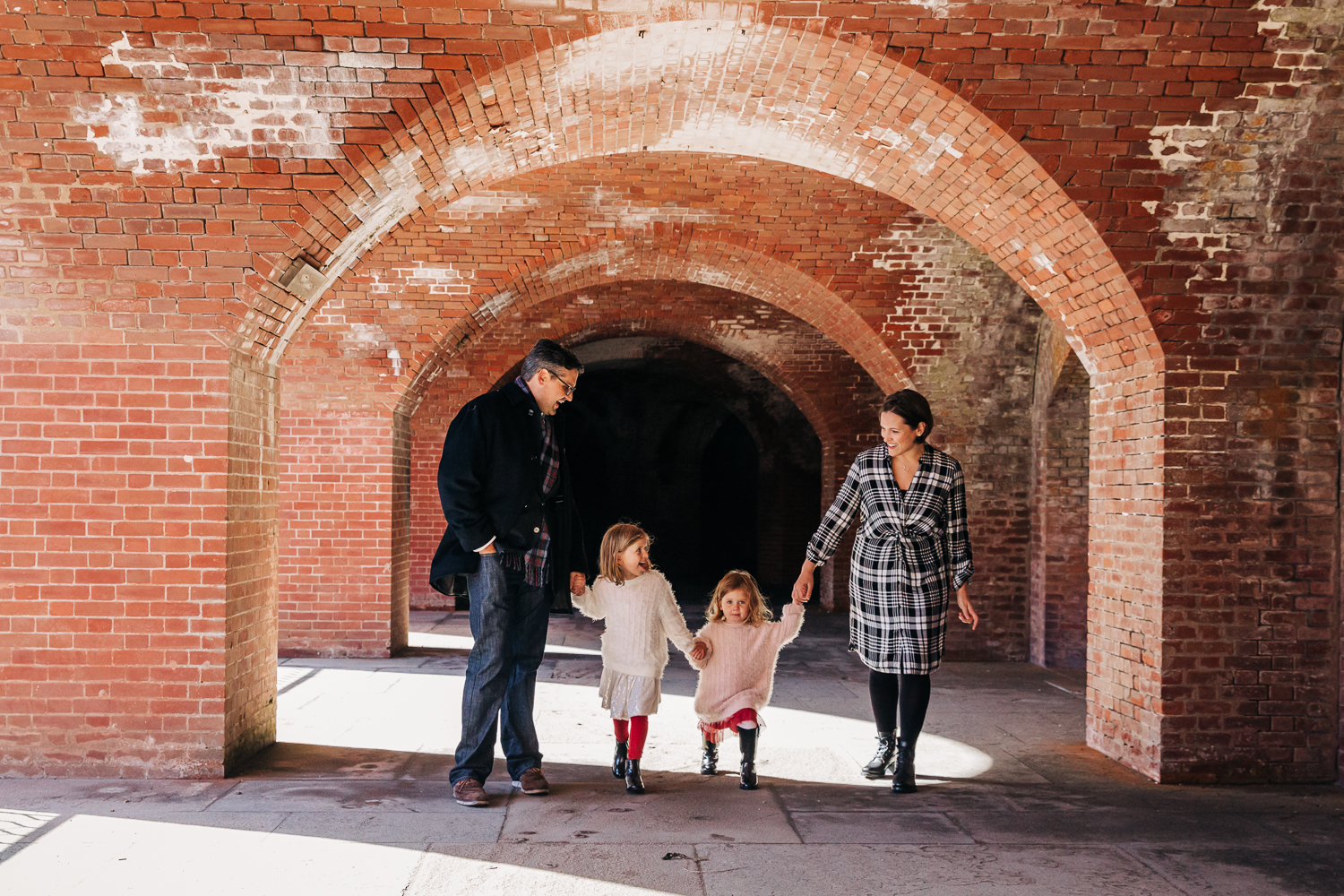 Family holding hands and walking together through an archway while looking at each other {Bay Area Family Photographer}