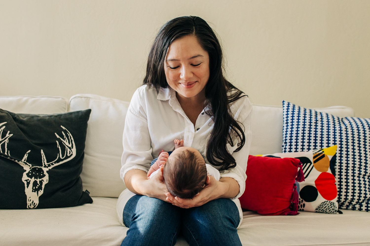 New Mother holding her new baby boy on her lap as she looks down at him smiling | San Francisco Newborn Photography