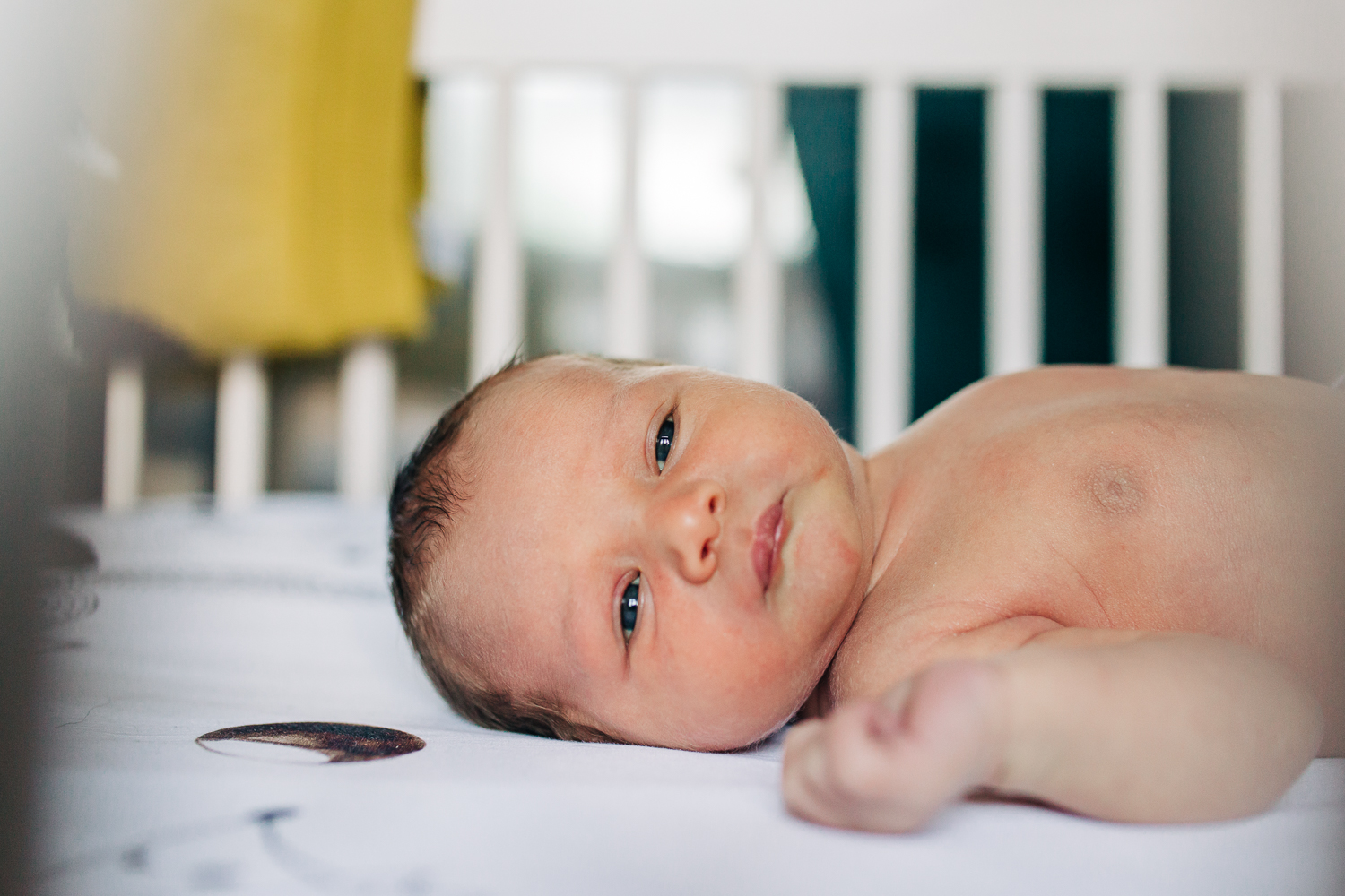 close up of baby boy laying in his crib and looking towards the camera | Bay Area Newborn Photographer