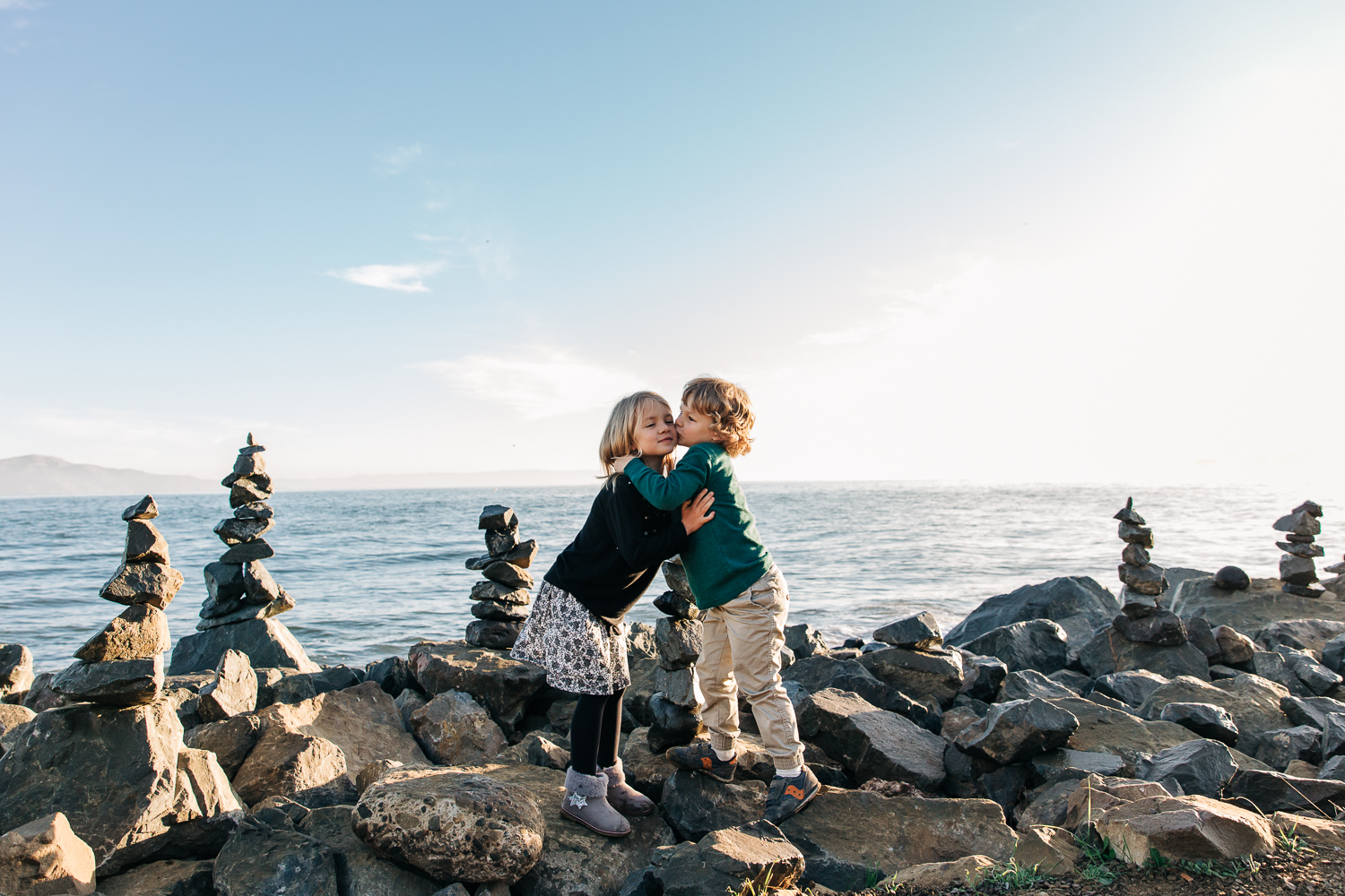 4 year old brother and 6 year old sister standing on rocks by the San Francisco Bay and hugging each other | Bay Area Family Photography