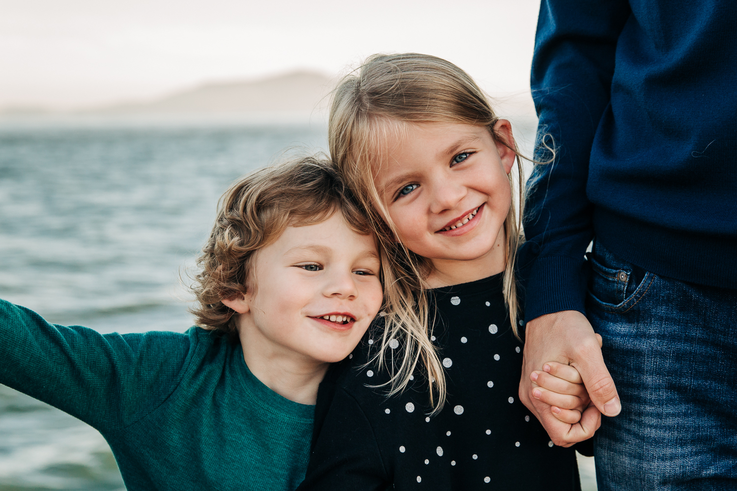 portrait of 4 year old brother and 6 year old sister snuggling while the little sister holds dad's hand | SF Bay Area Child Photographer