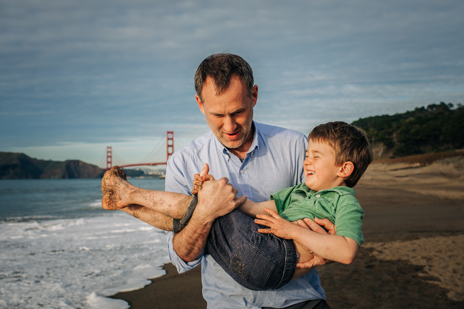 Dad holding his toddler son on the beach while they are both smiling | Bay Area Family Photography