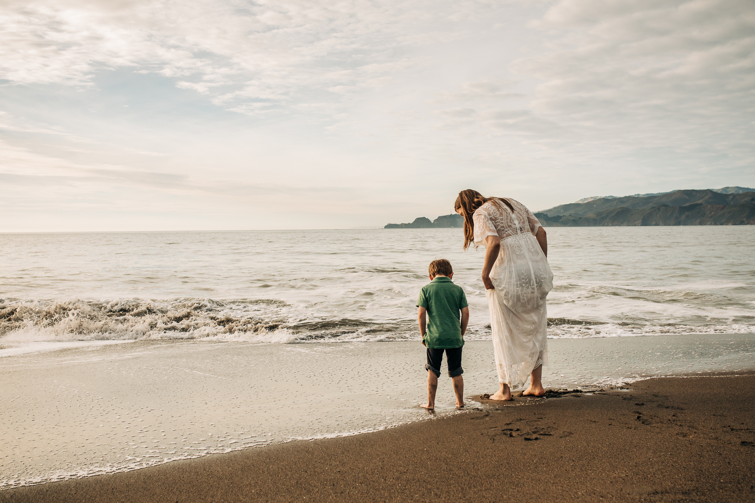 pregnant mother wading in the ocean at the beach with her toddler son | Bay Area Maternity Photographer