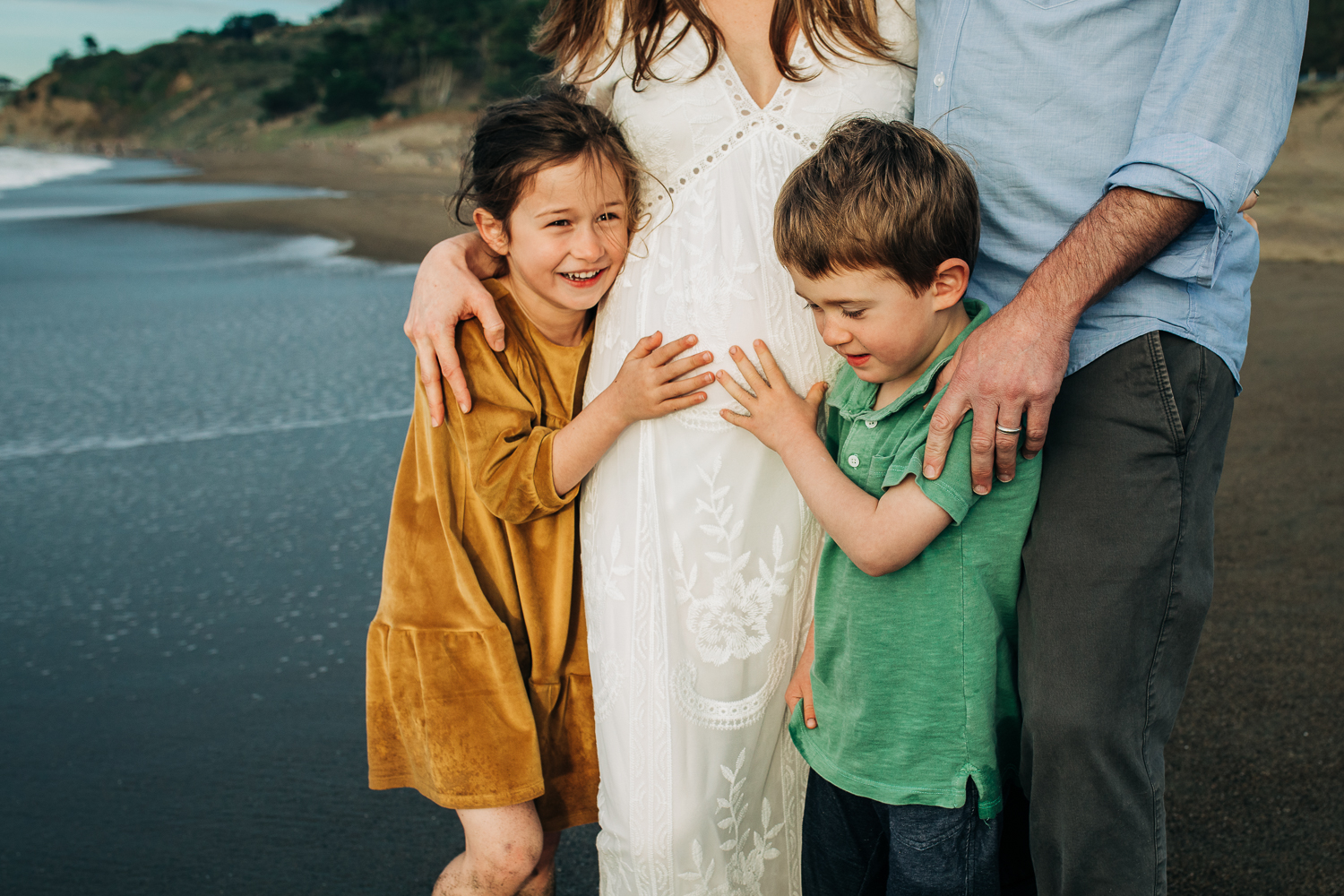 a boy and a girl standing in front of their parents with their hands on their mother's baby bump | Easy Bay Maternity Photographer