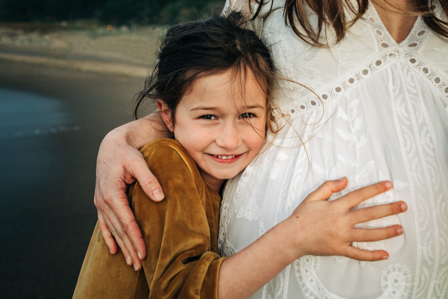 little girl smiling at the camera and snuggling her pregnant mother close and touching her mother's baby bump | San Francisco Baby Photographer