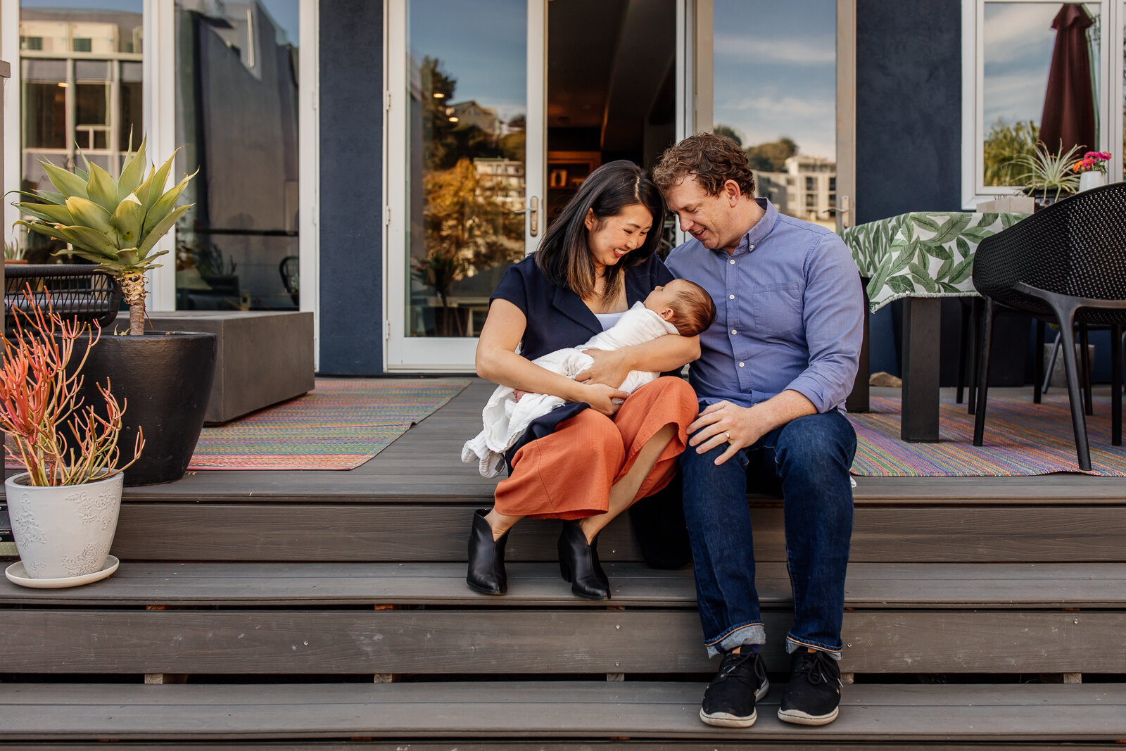 parents sitting on stairs of back deck holding baby boy - Oakland Newborn Photographer