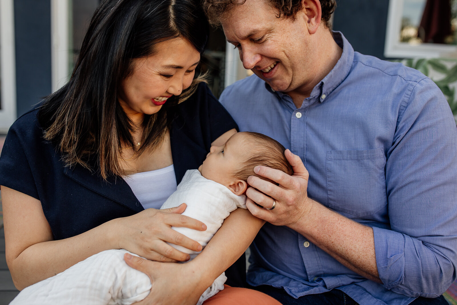 parents looking down and smiling while mom holds new baby - Bay Area Newborn Photographer