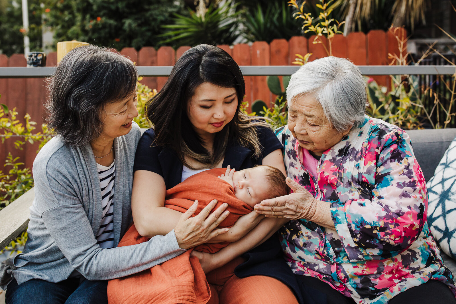 grandmother, great-grandmother, daughter and grandson all sitting together and looking down at baby boy - Oakland Newborn Photographer