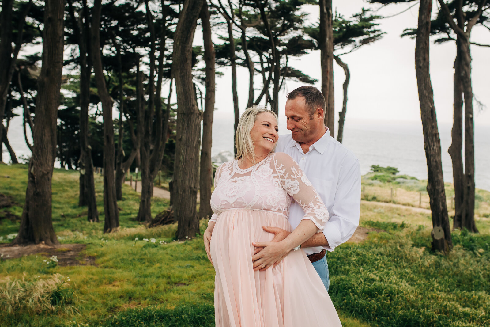 pregnant wife turning towards her husband as he stands behind her and embracing her belly - San Francisco Maternity Photographer