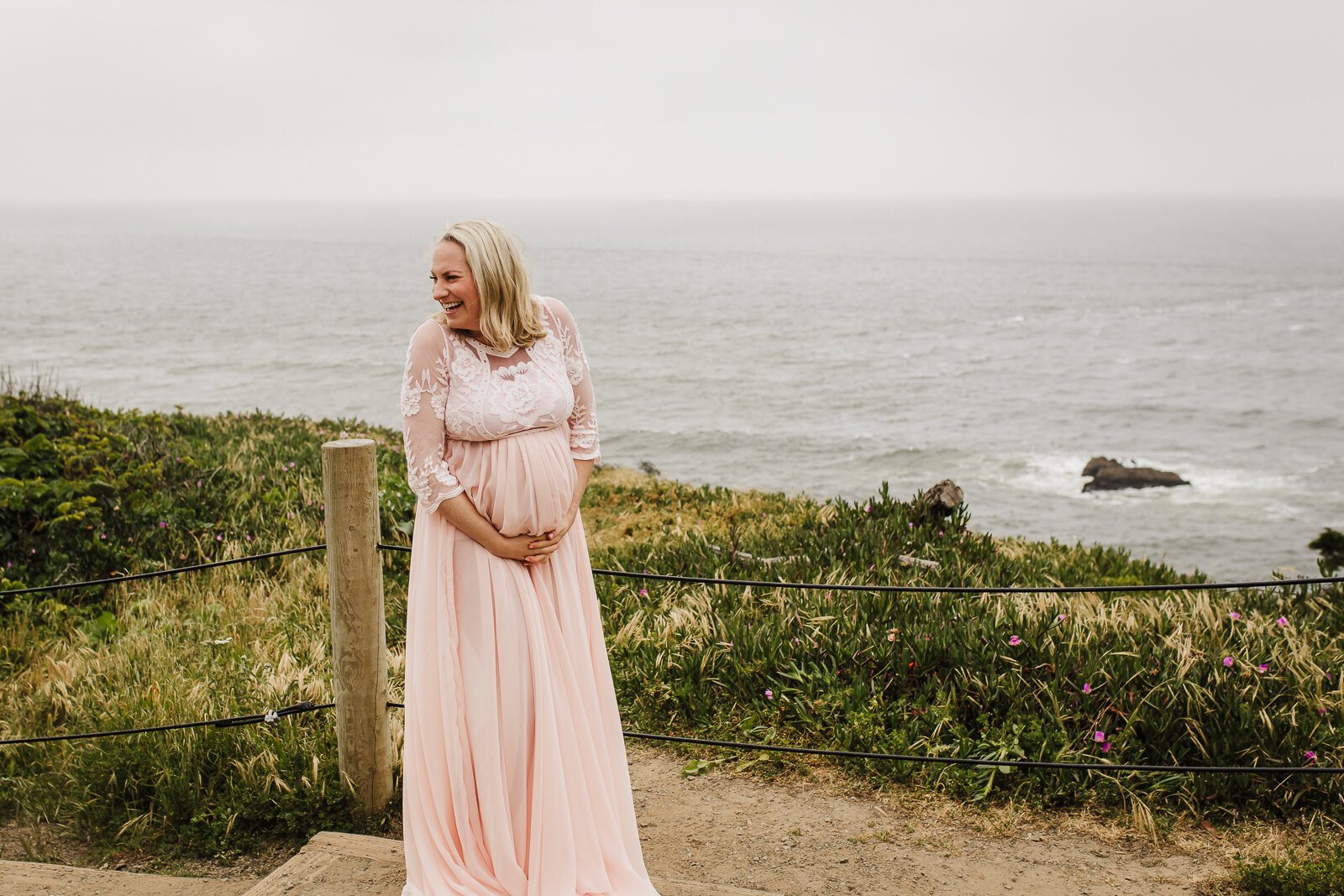 pregnant mom looking over her shoulder and laughing while standing with the ocean behind her - San Francisco Maternity Photographer