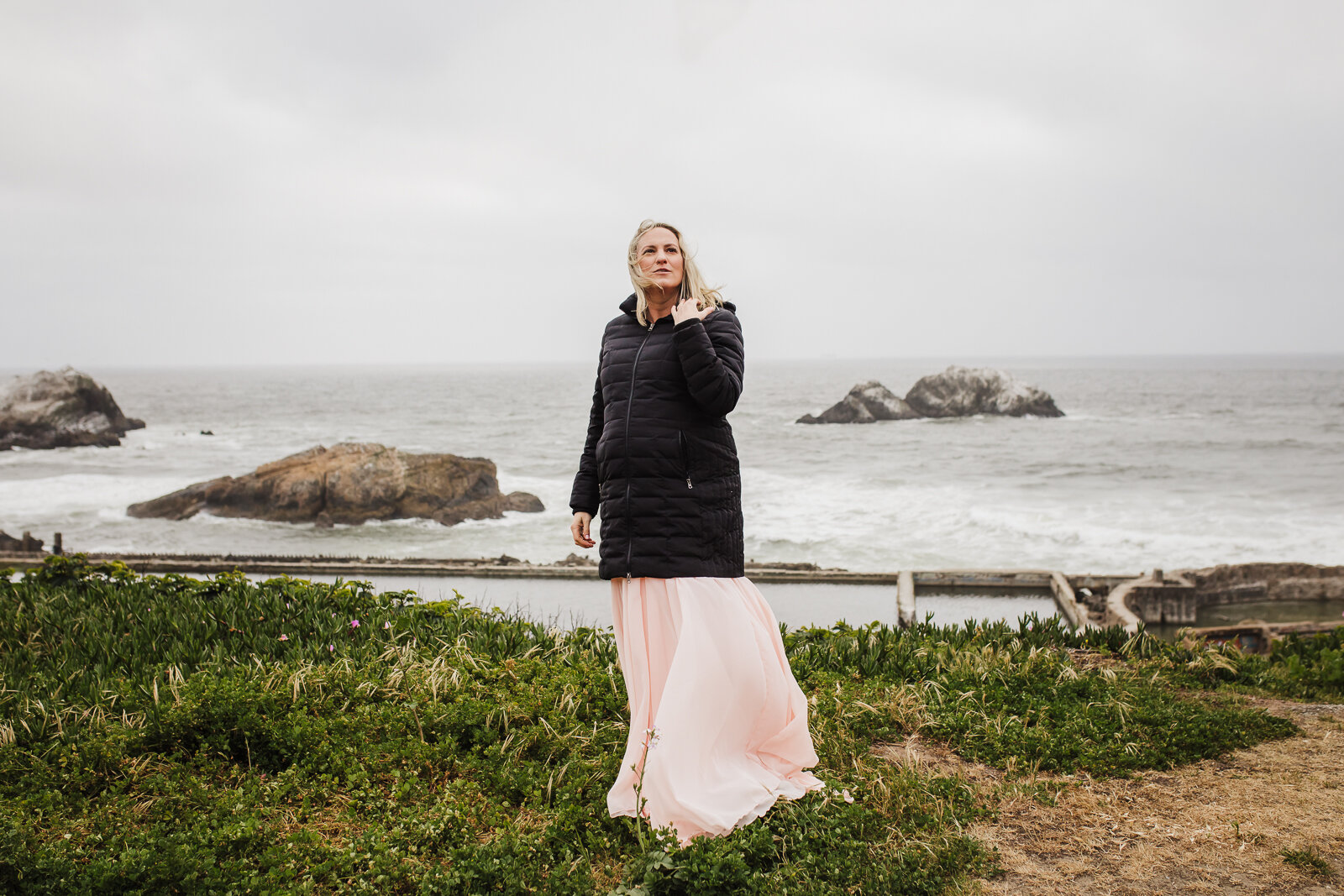 pregnant mom staying warm with a jacket while her dress blows in the wind - San Francisco Maternity Photographer
