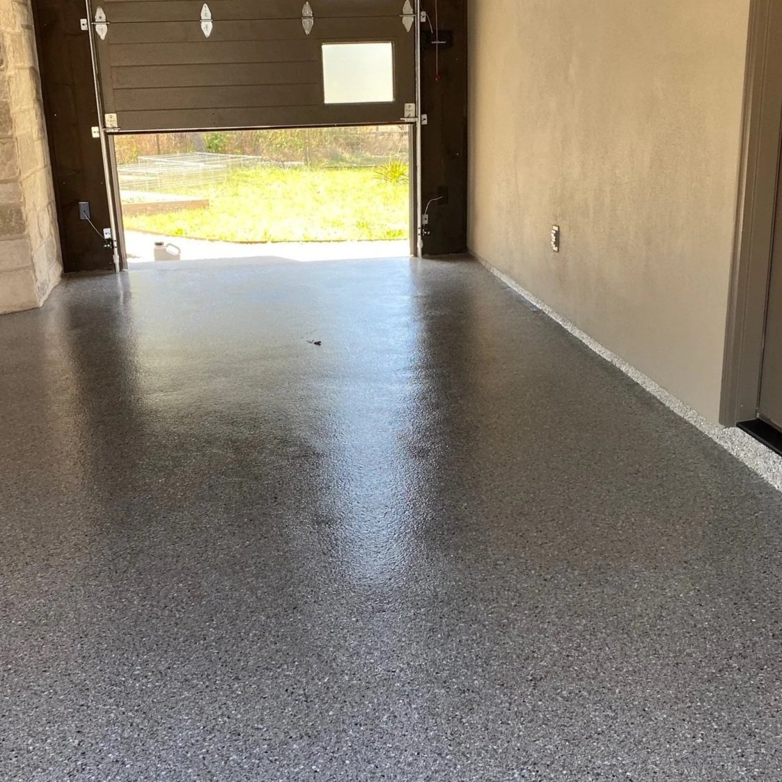 A refinished resinous coating garage floor in front of a roll up garage door.