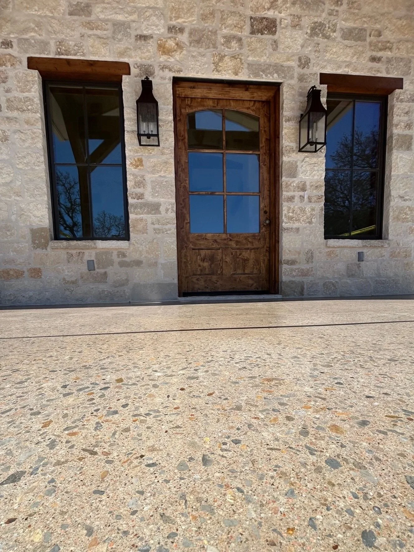 Hybrid-stone travertine epoxy replicating natural stone elements on a front porch of a house with a wooden door and 2 windows near Hext, TX