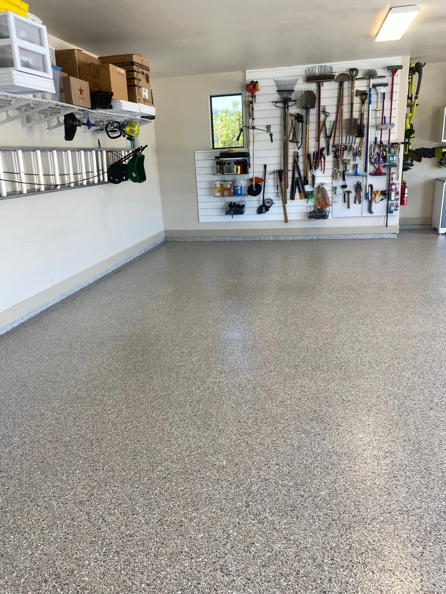 Inside of a garage with a ladder and tools hanging on walls above a newly refinished concrete floor with a resinous coating.