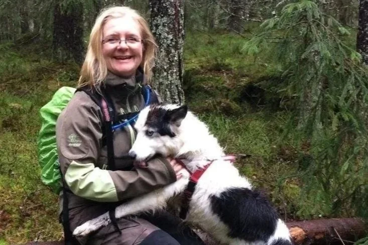 En kvinne smiler og holder en hund i en skog