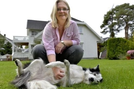 Kvinne som leker med en stor, svart-hvit hund på en grønn plen foran et hvitt hus.