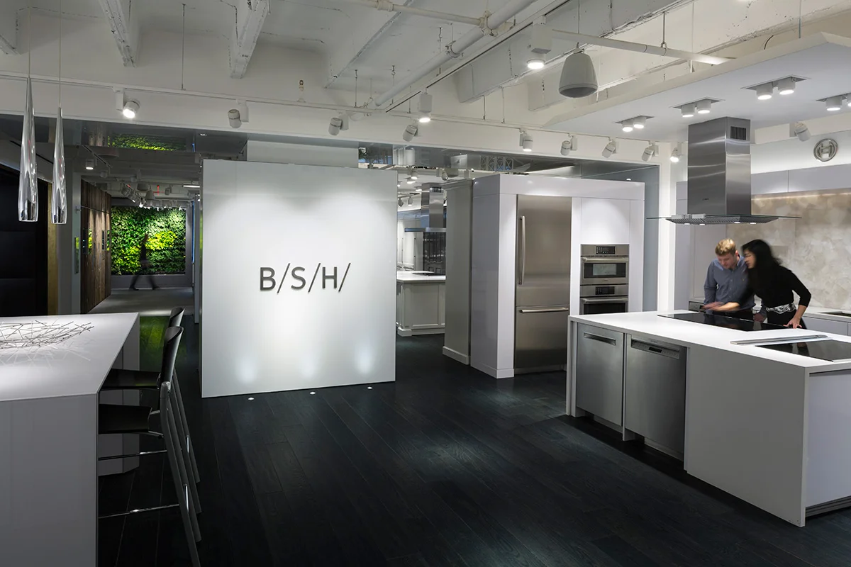 BSH logo displayed on a wall as a man and woman explore the showroom's kitchen space in New York. MEP provided by 2L Engineering.