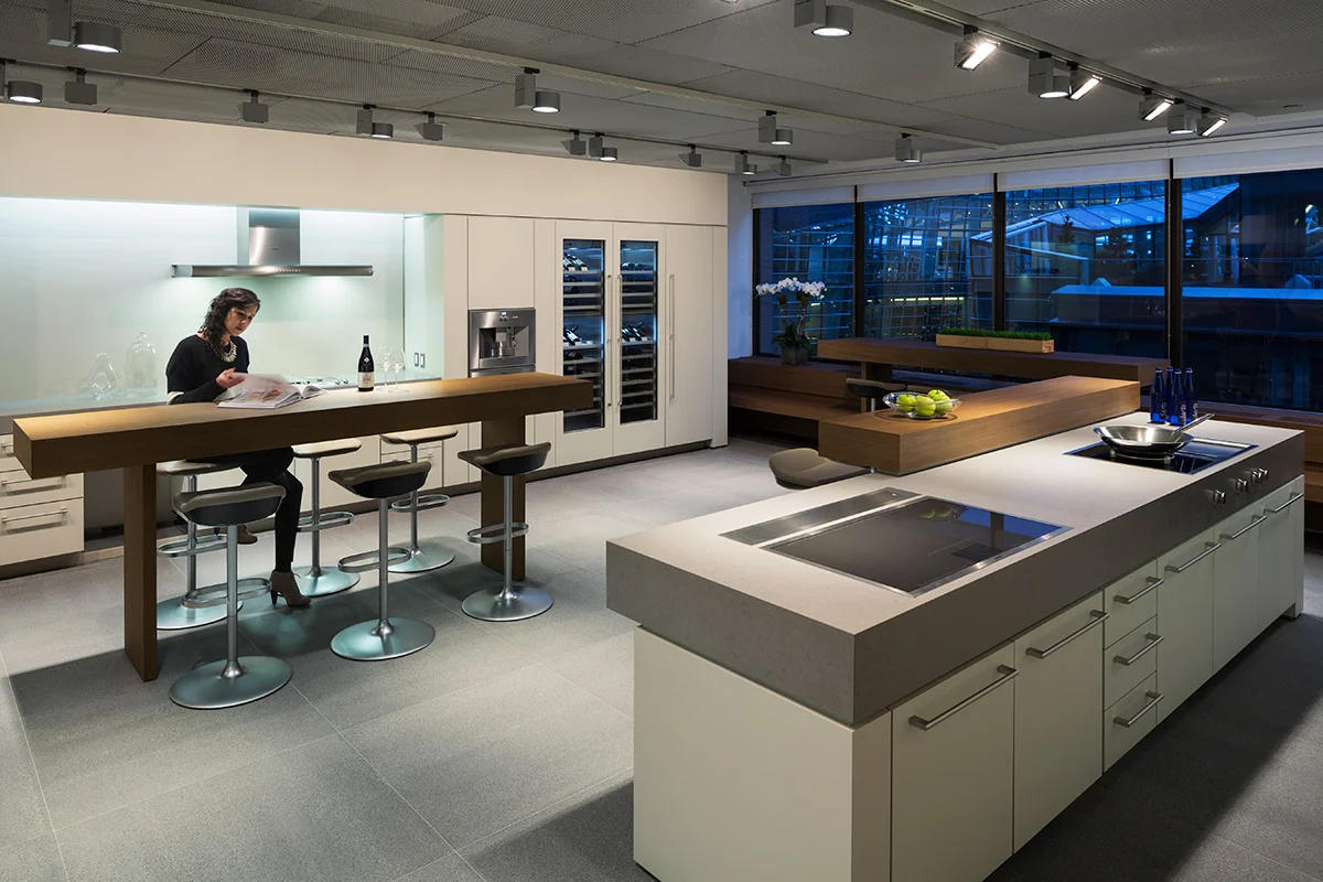 A woman reviewing a catalog as she sits at a wooden kitchen island in the middle of a showroom at BSH. MEP by New York based firm, 2L Engineering.